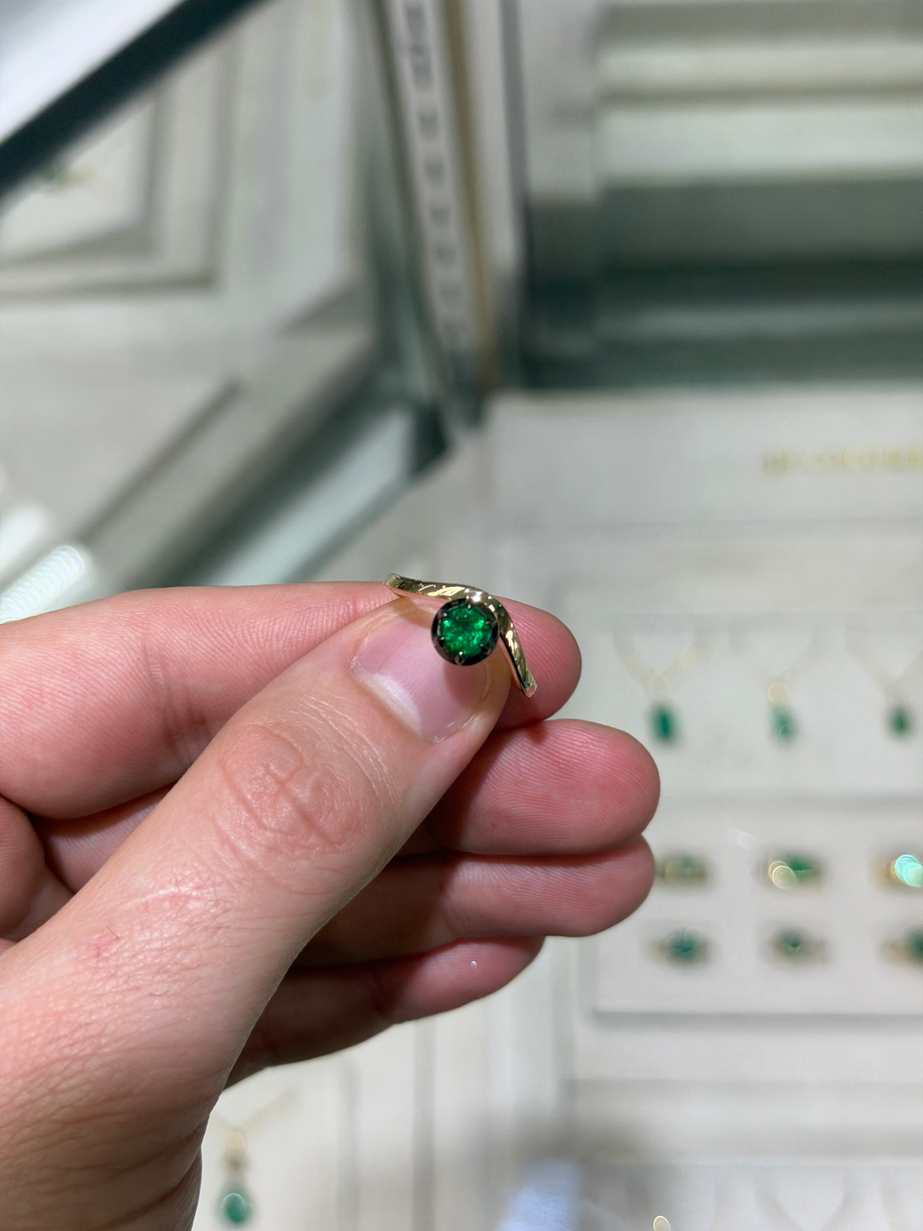 Ladies emerald ring featuring a 0.64ct natural round cut emerald in a multi-prong 14K gold setting with black rhodium finish.