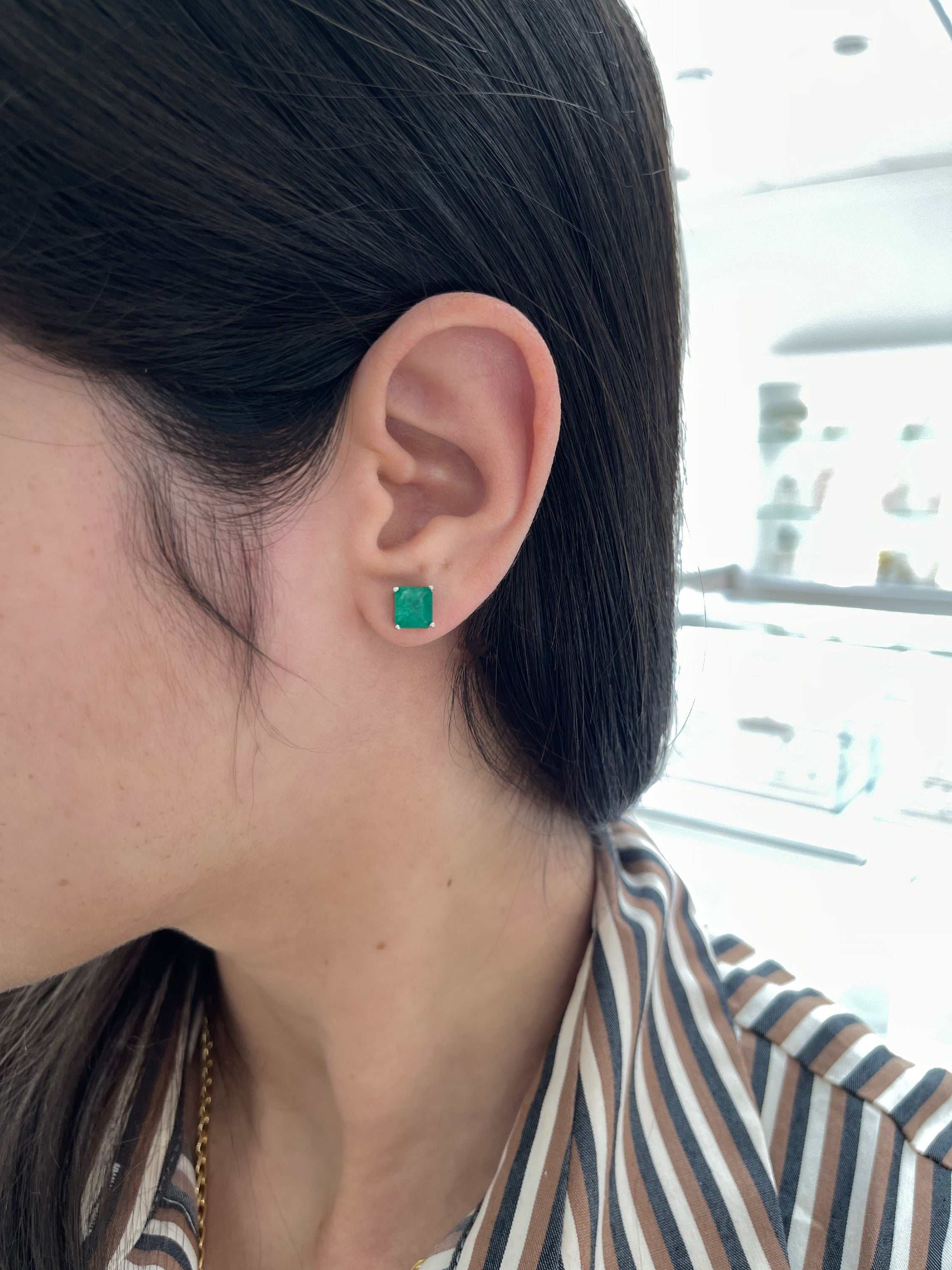 Earthy deep green Colombian emerald stud earrings in 14K white gold on ear.