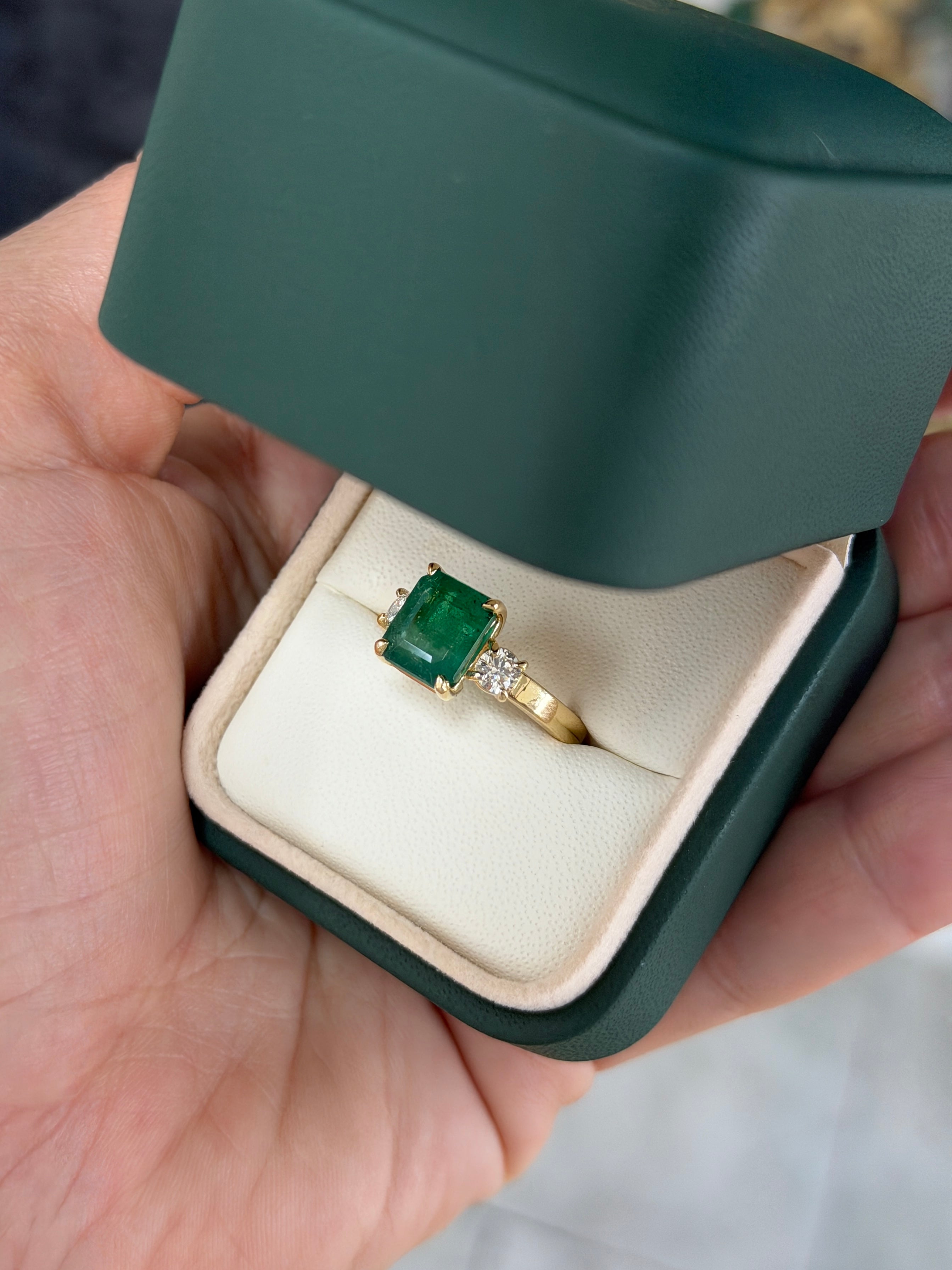 Zambian emerald cut three stone engagement ring with round diamond side stones in 14K gold, featuring the JR Colombian Emeralds brand.