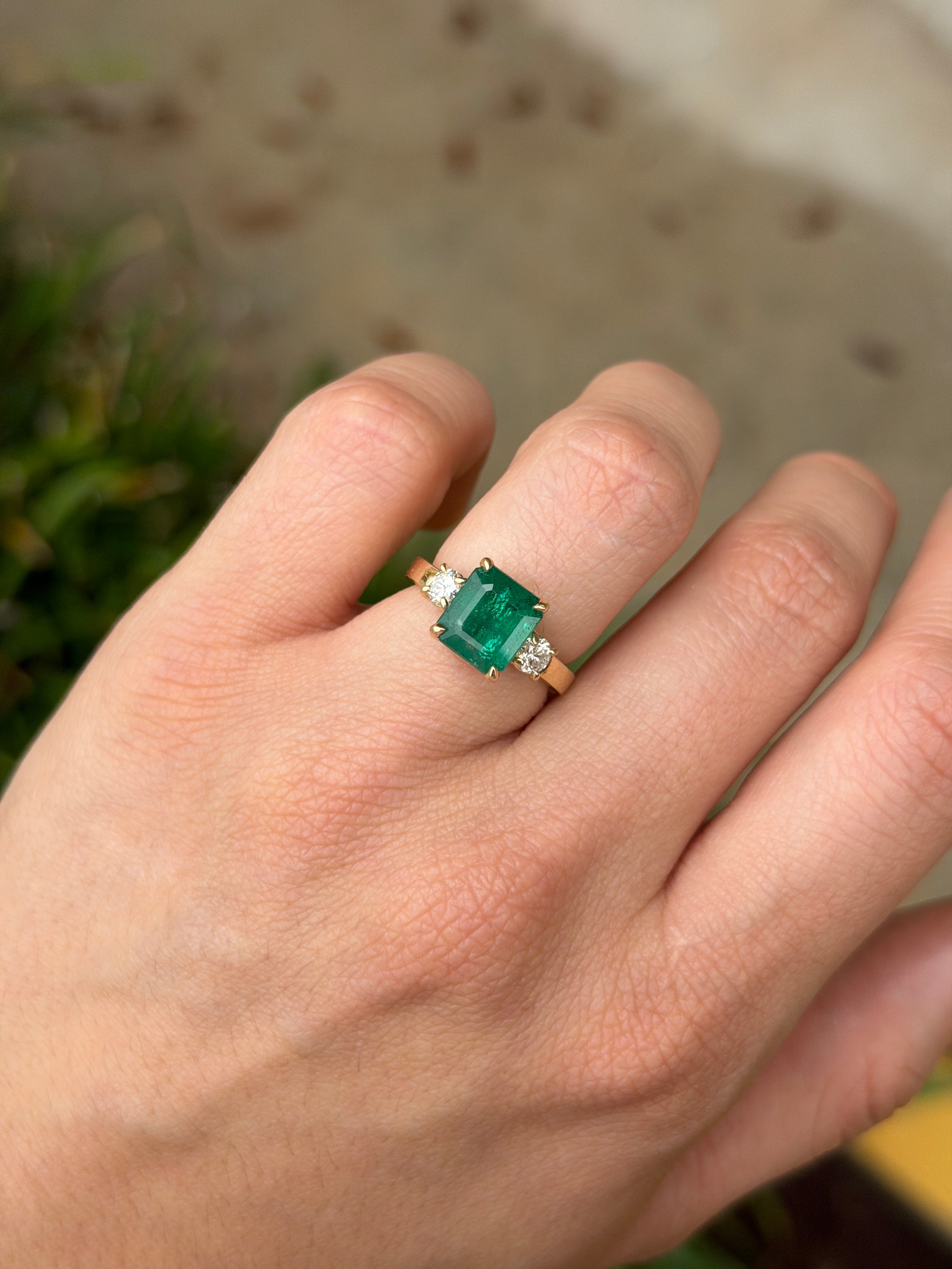 Zambian emerald cut three stone engagement ring with round diamond side stones in 14K gold featuring the JR Colombian Emeralds brand.