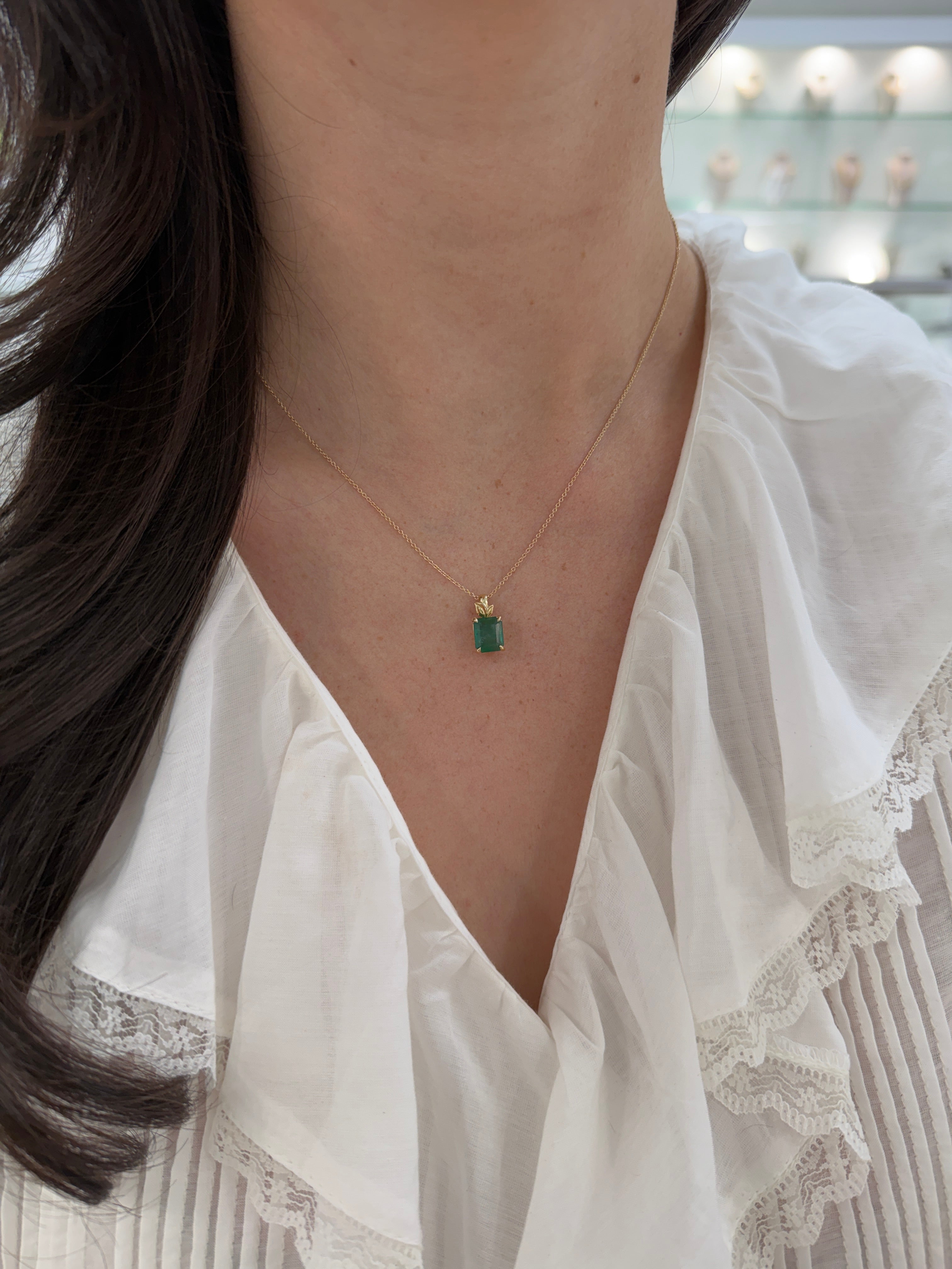Emerald cut emerald pendant by JR Colombian Emeralds featuring a leaf-shaped design with 14K gold bail and chain.