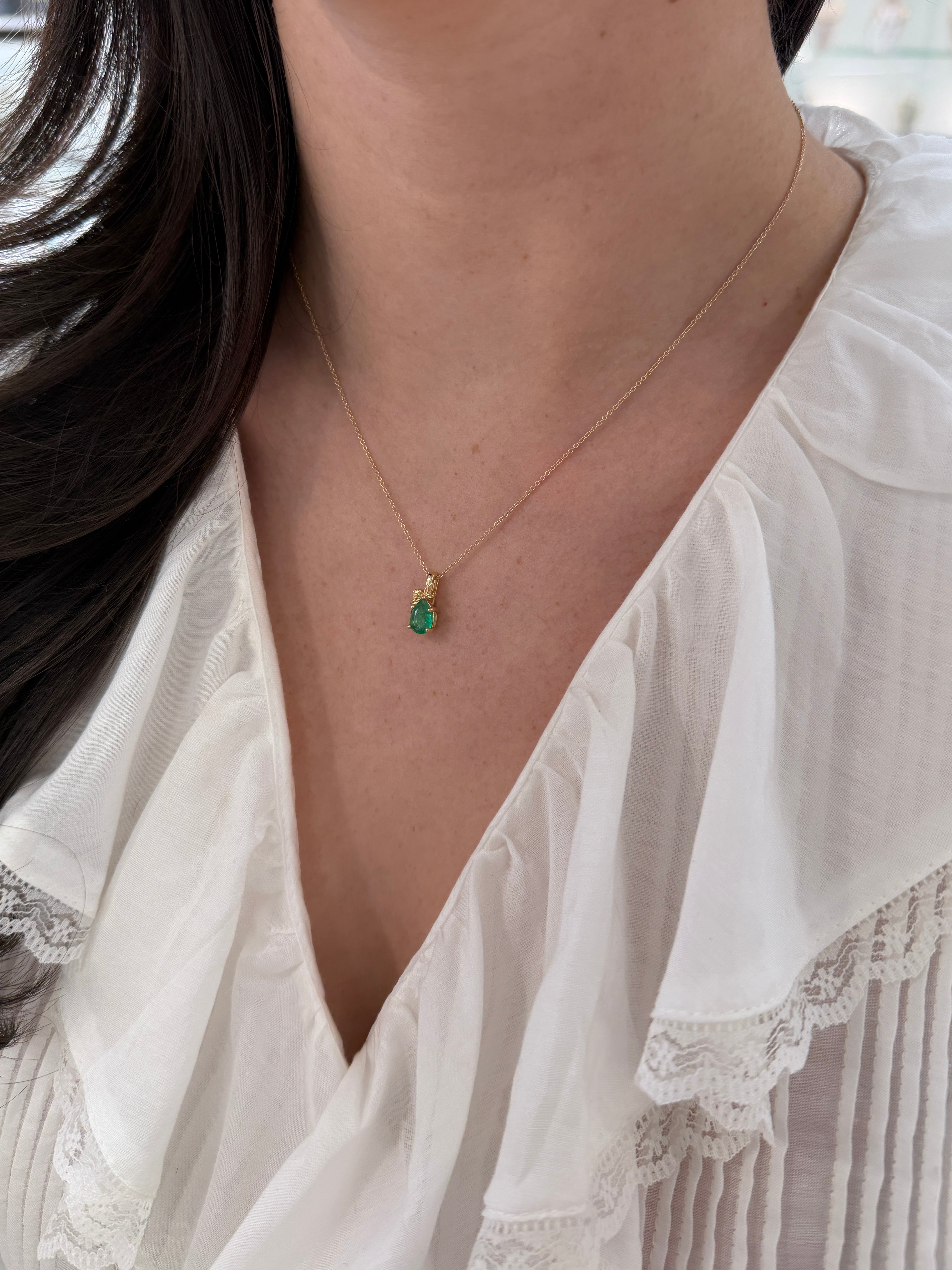 14K gold pendant necklace featuring a 1.0ct natural medium green pear-shaped emerald set in a floral solitaire design.