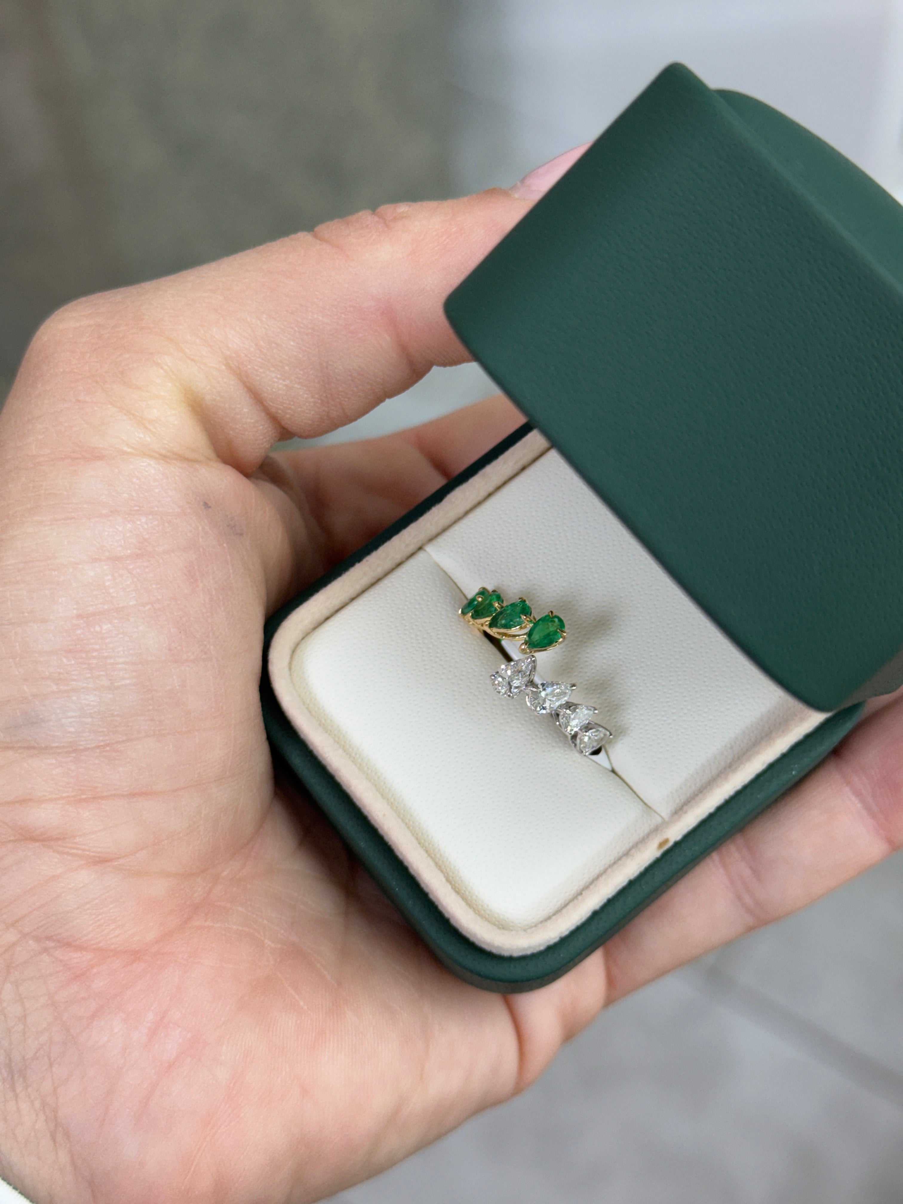 Two toned bypass 18K gold band with pear-shaped emerald and diamond stones in a green jewelry box