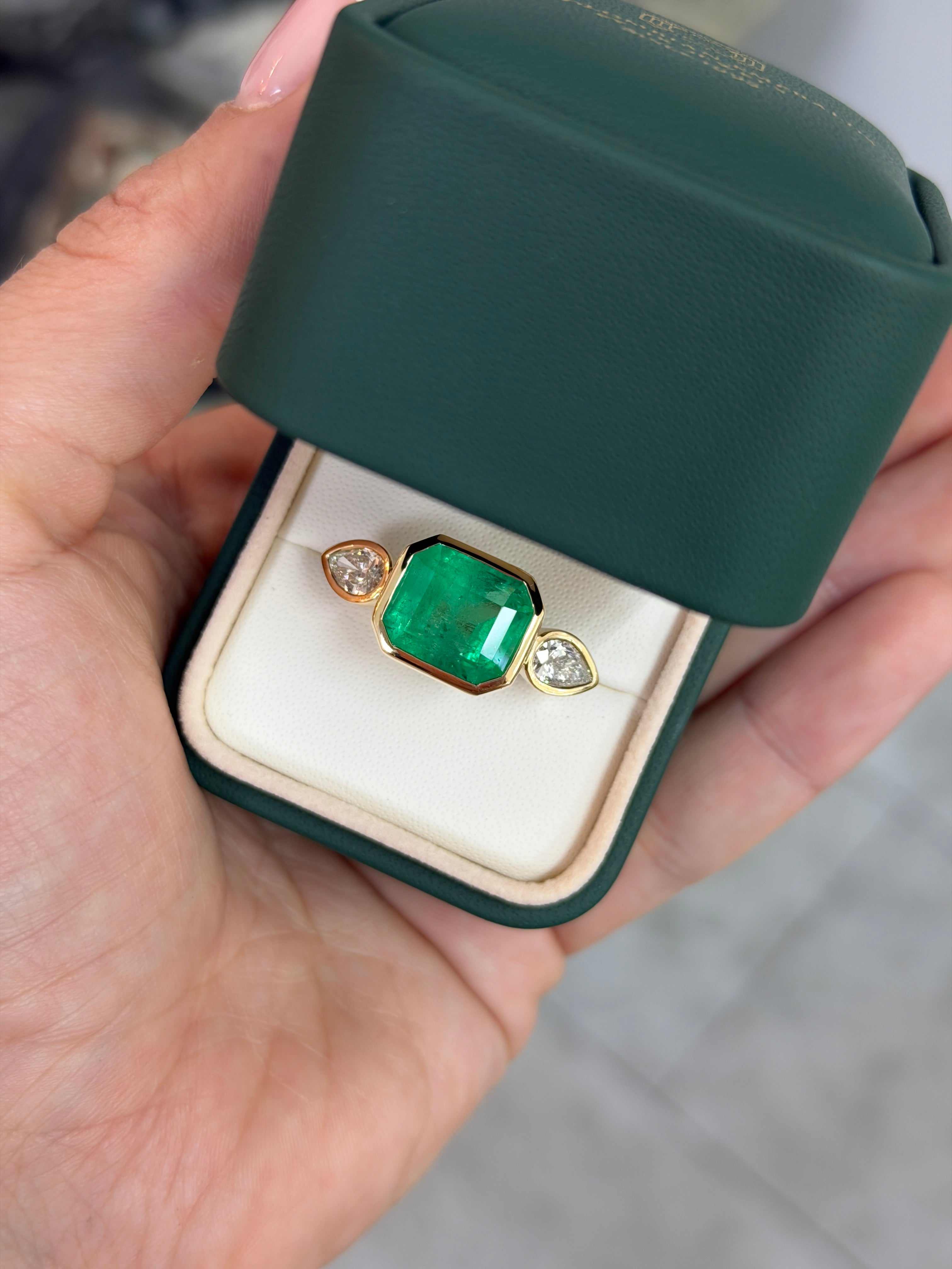 18K yellow gold bezel ring with 9.74-carat emerald cut East to West Colombian emerald and pear cut diamond three stone setting