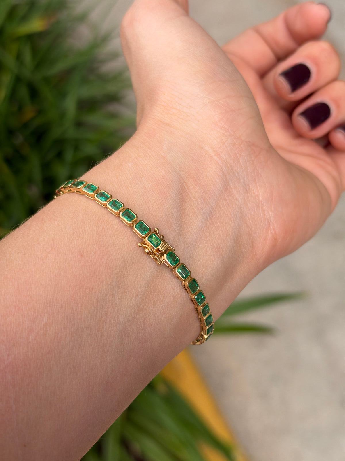 14K gold emerald tennis bracelet with bezel-set green emeralds totaling 6.69 carats, designed in an east-to-west style.