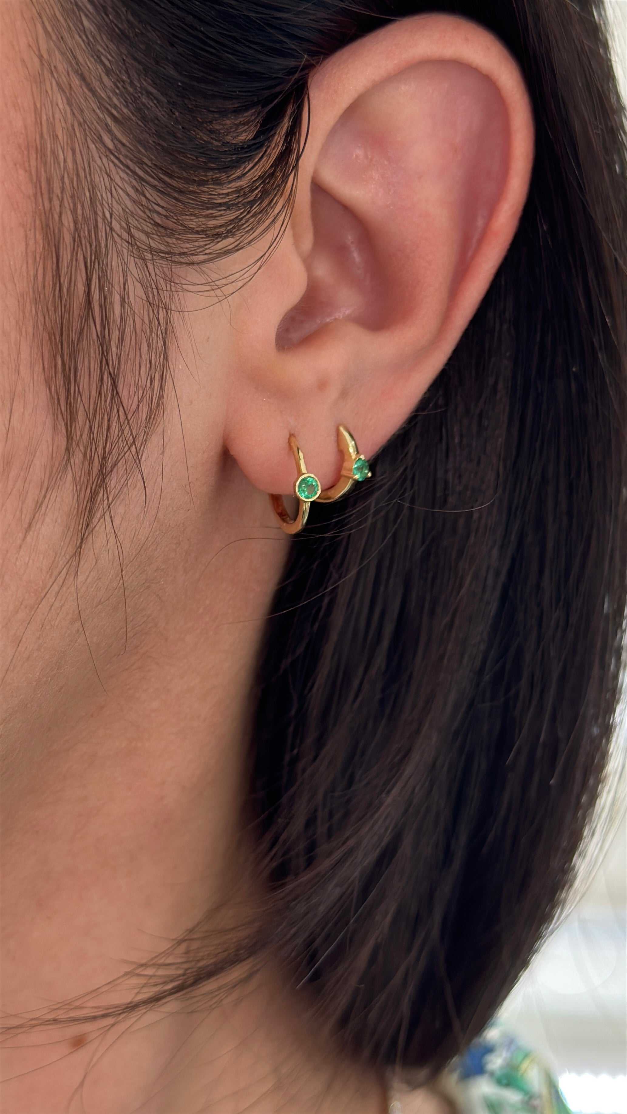Emerald huggie earring by JR Colombian Emeralds featuring three-prong setting in 14K gold, close-up view of the jewelry.
