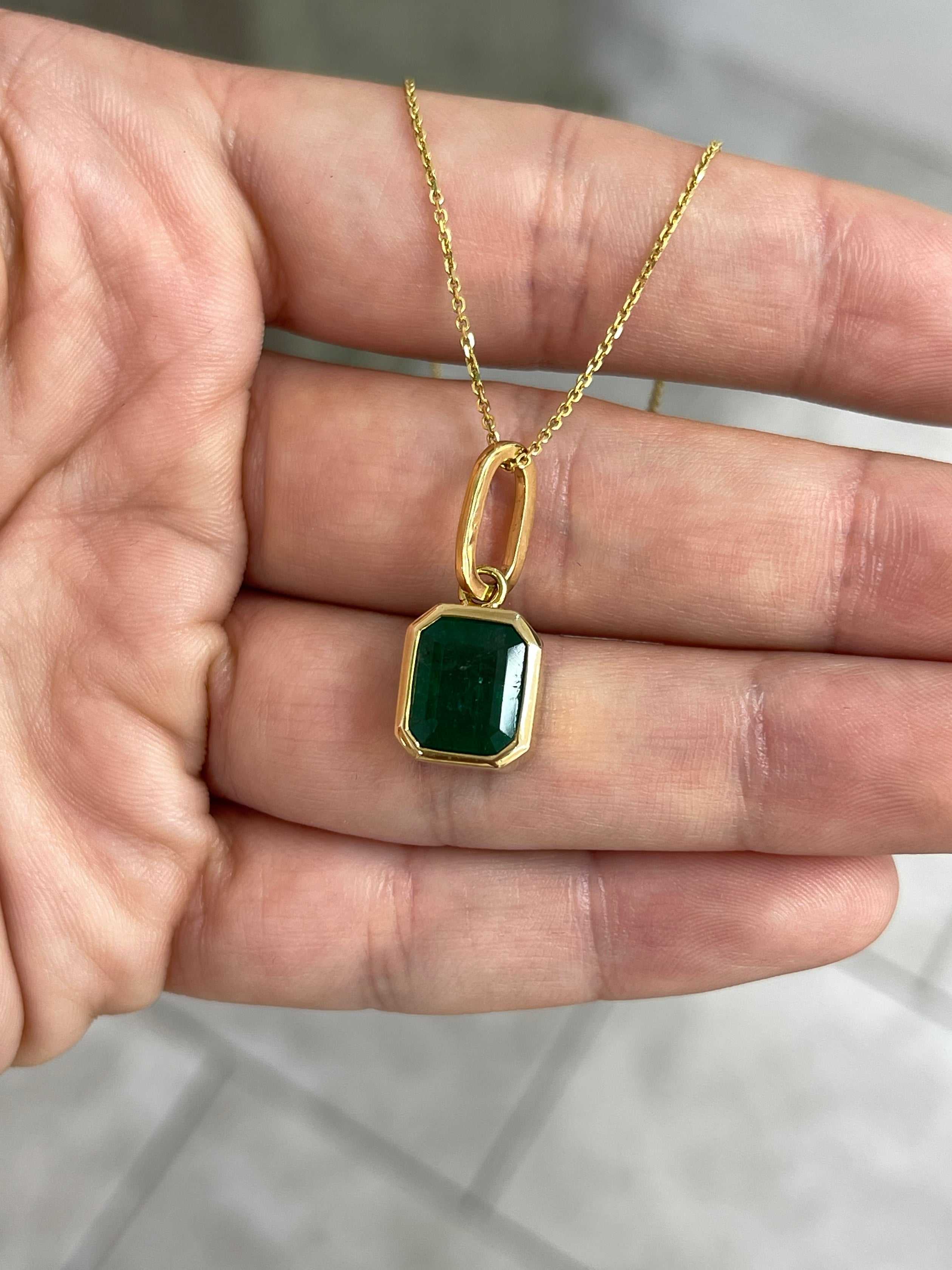 Dark green Zambian emerald necklace with 4.98 carat bezel-set emerald pendant in 14K gold, featuring intricate detailing and chain.