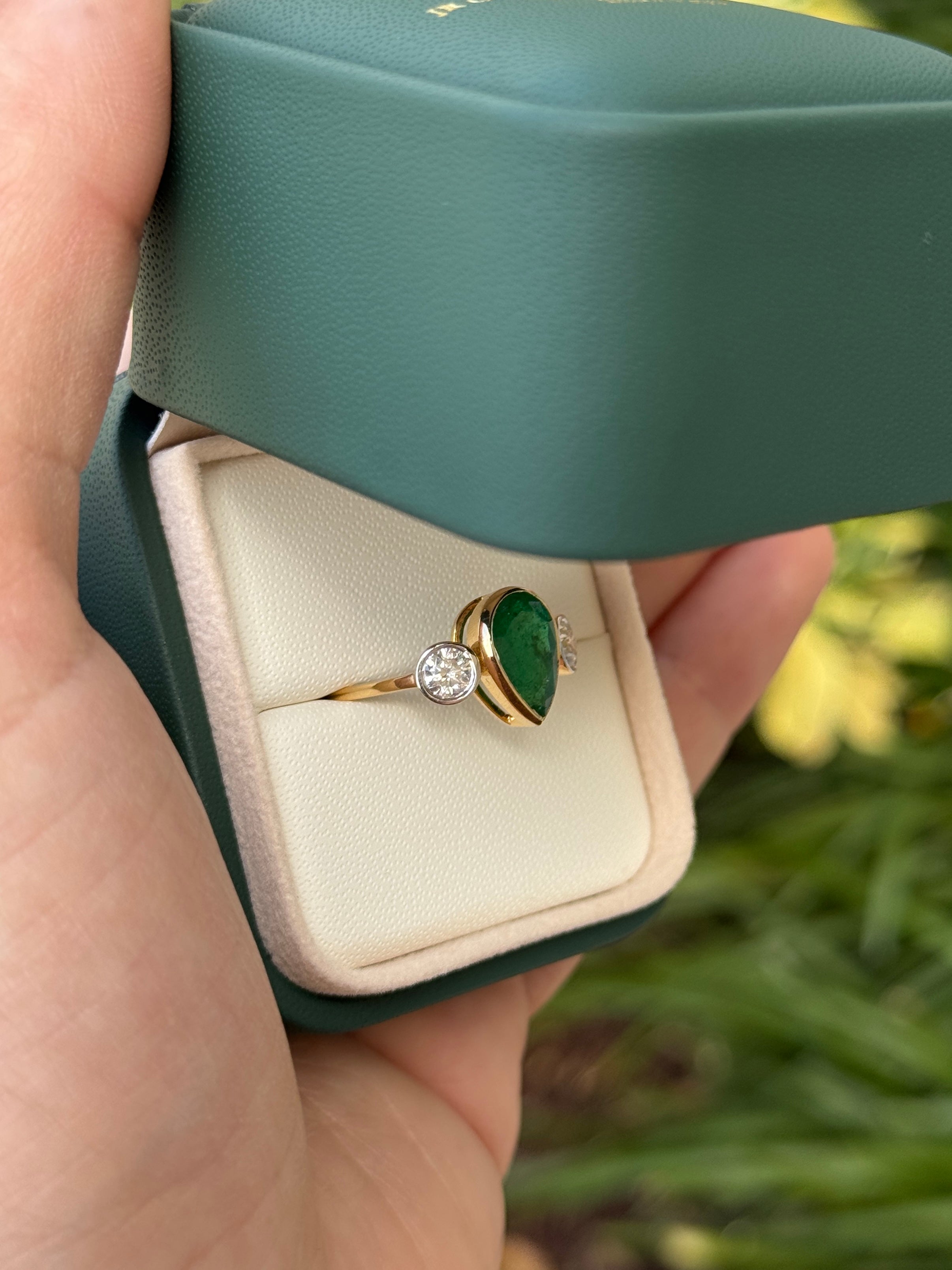 Pear-shaped emerald three-stone ring with round diamond accents in 18K yellow gold, featuring 2.91 carats total weight.