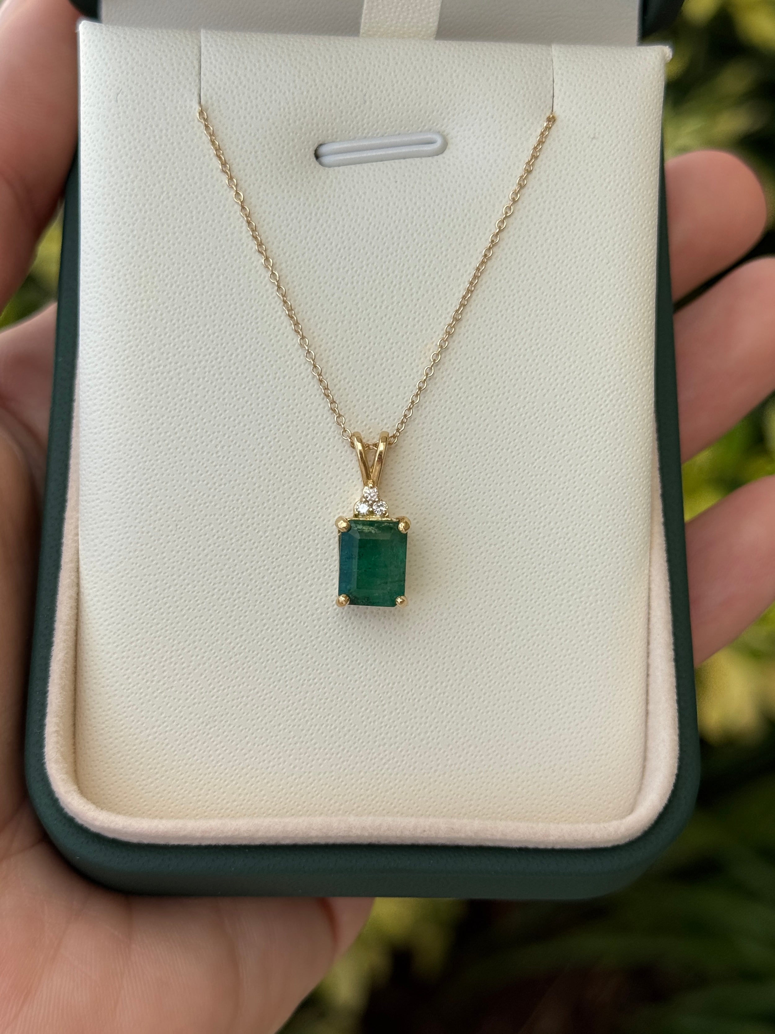 Emerald cut emerald pendant with trefoil diamond accents in 14K gold, showcasing vibrant green gemstone and sparkling details.