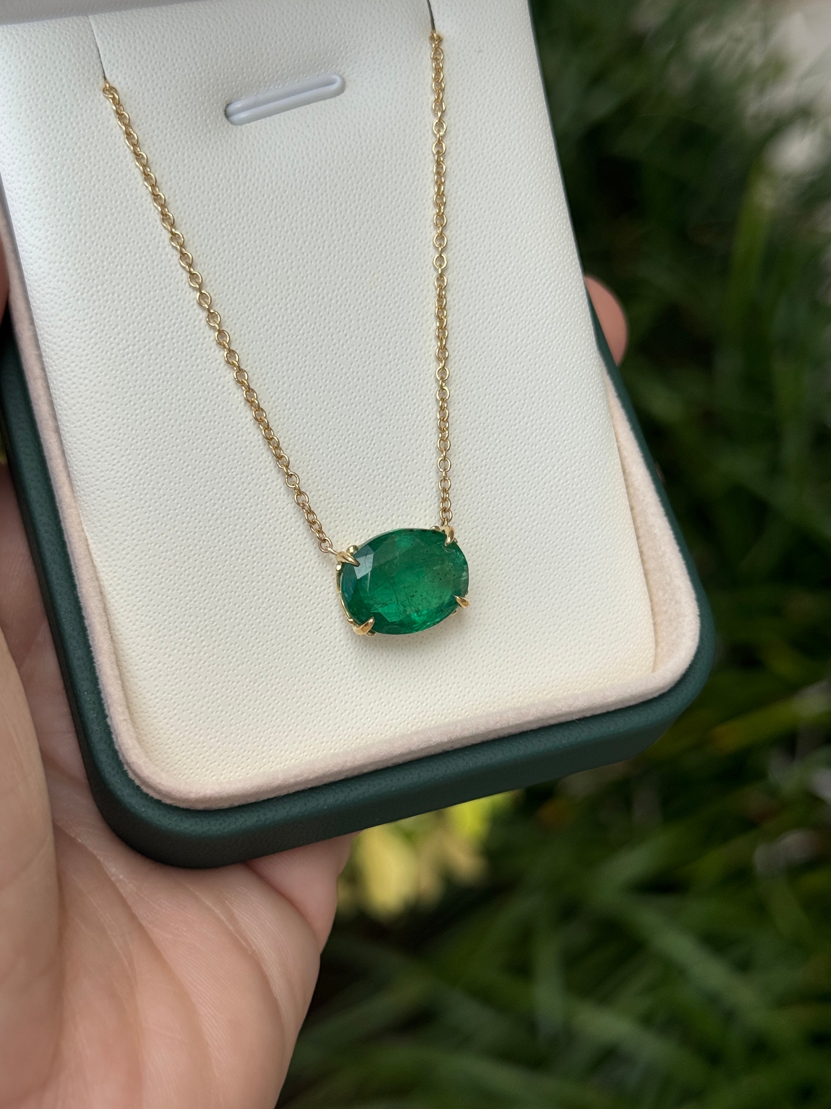 18K gold emerald necklace featuring a 6.80 carat oval natural emerald Fleur De Lis pendant, styled in a stationary station design.