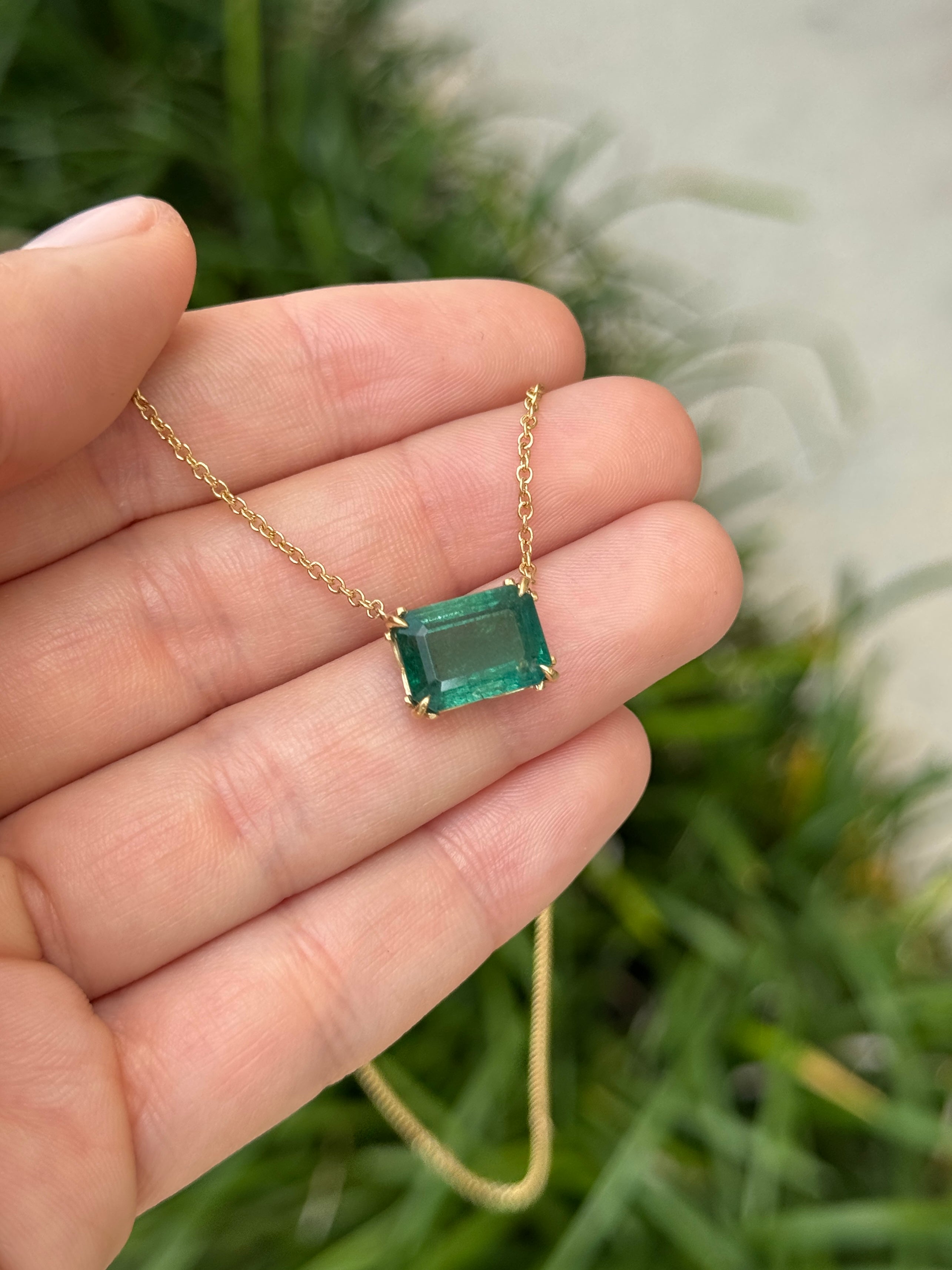 18K gold emerald solitaire necklace featuring a 5.70ct east-west stationary emerald in floral fleur de lis design by JR Colombian Emeralds.