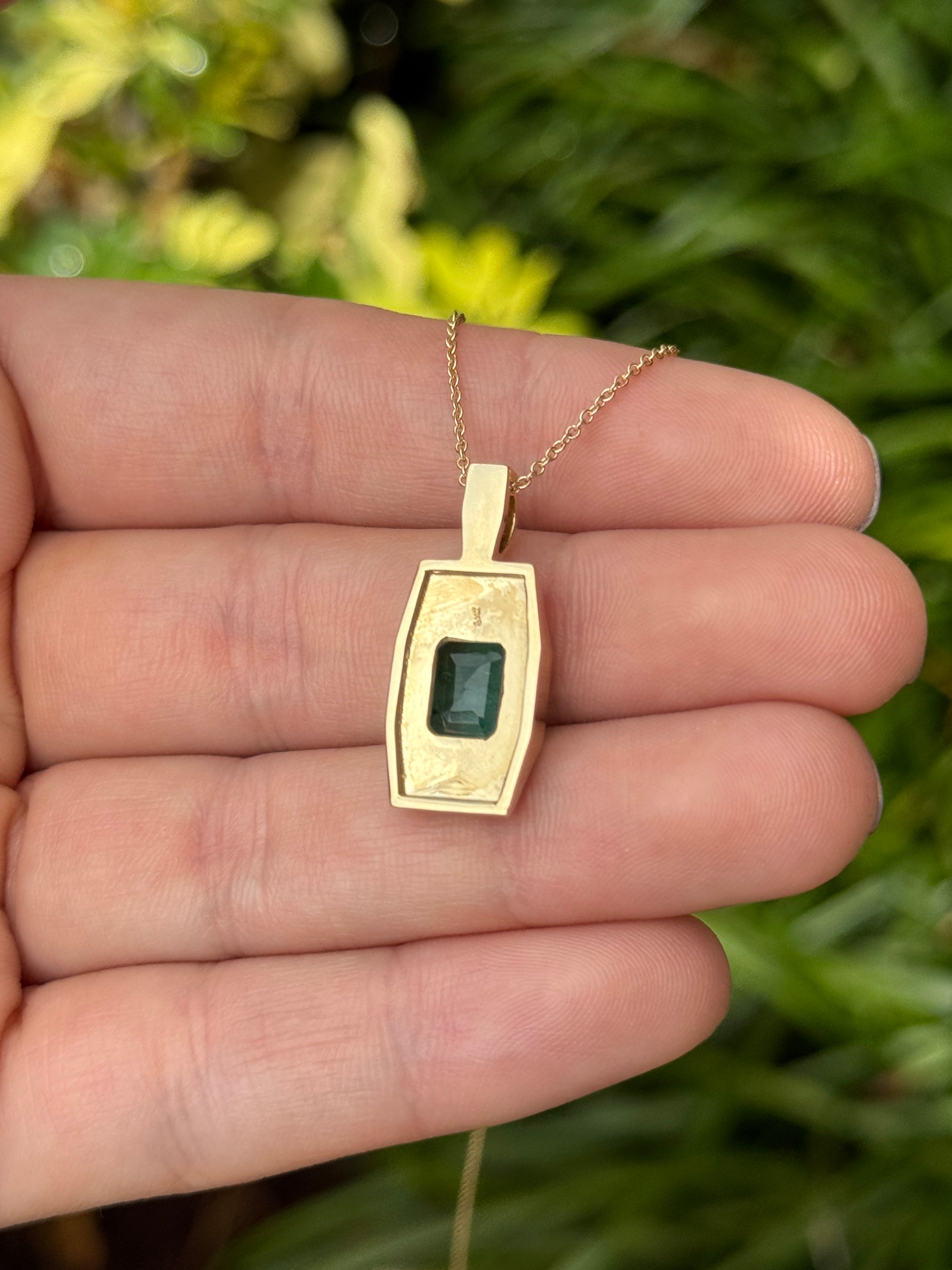 14K gold emerald dog tag pendant featuring a 2.35 carat rectangular Colombian emerald, engraved details, and polished finish.