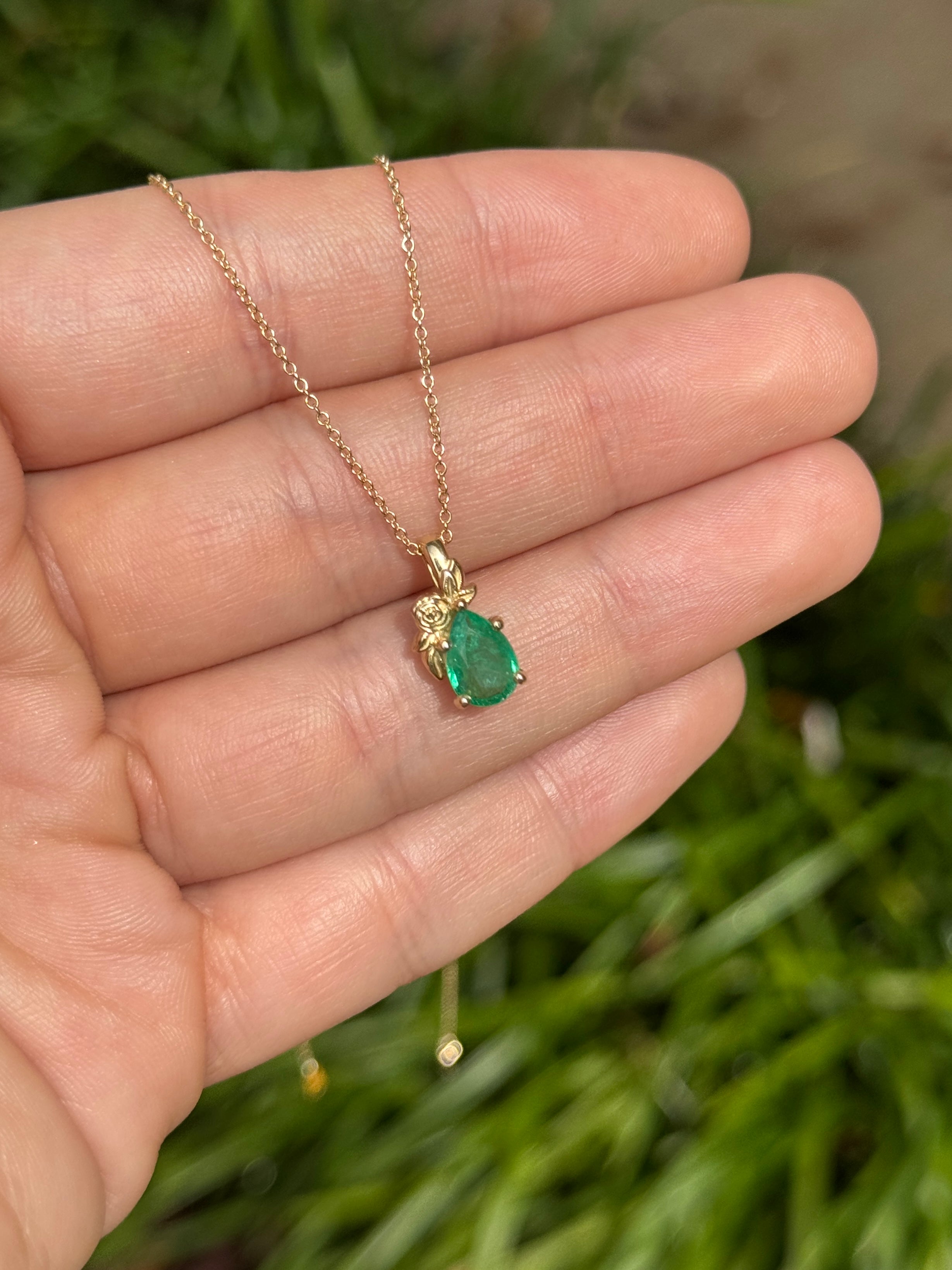 Natural medium green pear cut emerald set in floral solitaire pendant necklace with 14K gold, featuring a sparkling design.