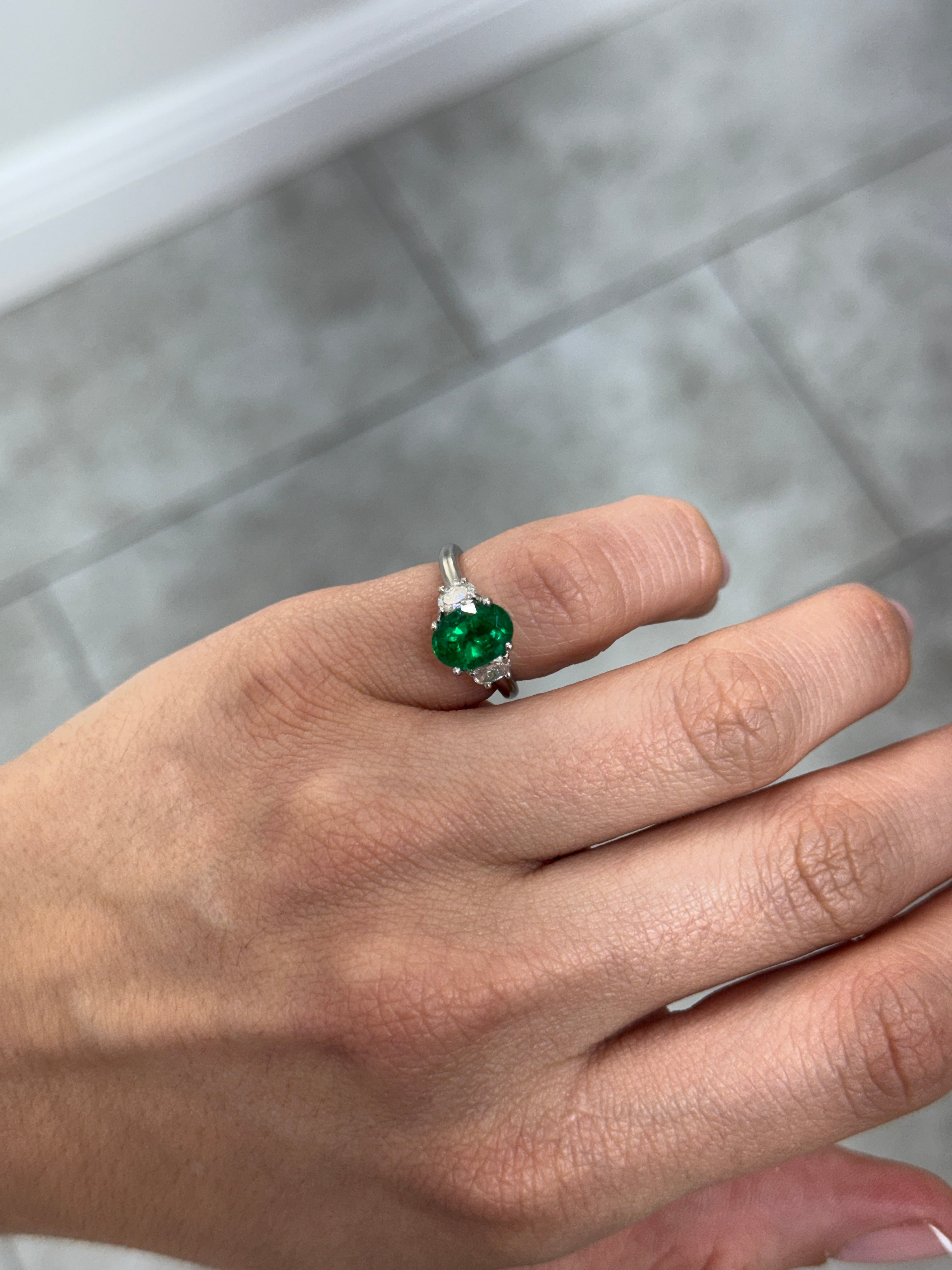 Vivid green oval emerald and oval diamond three-stone ring in platinum by JR Colombian Emeralds, showcasing elegant gemstone details.