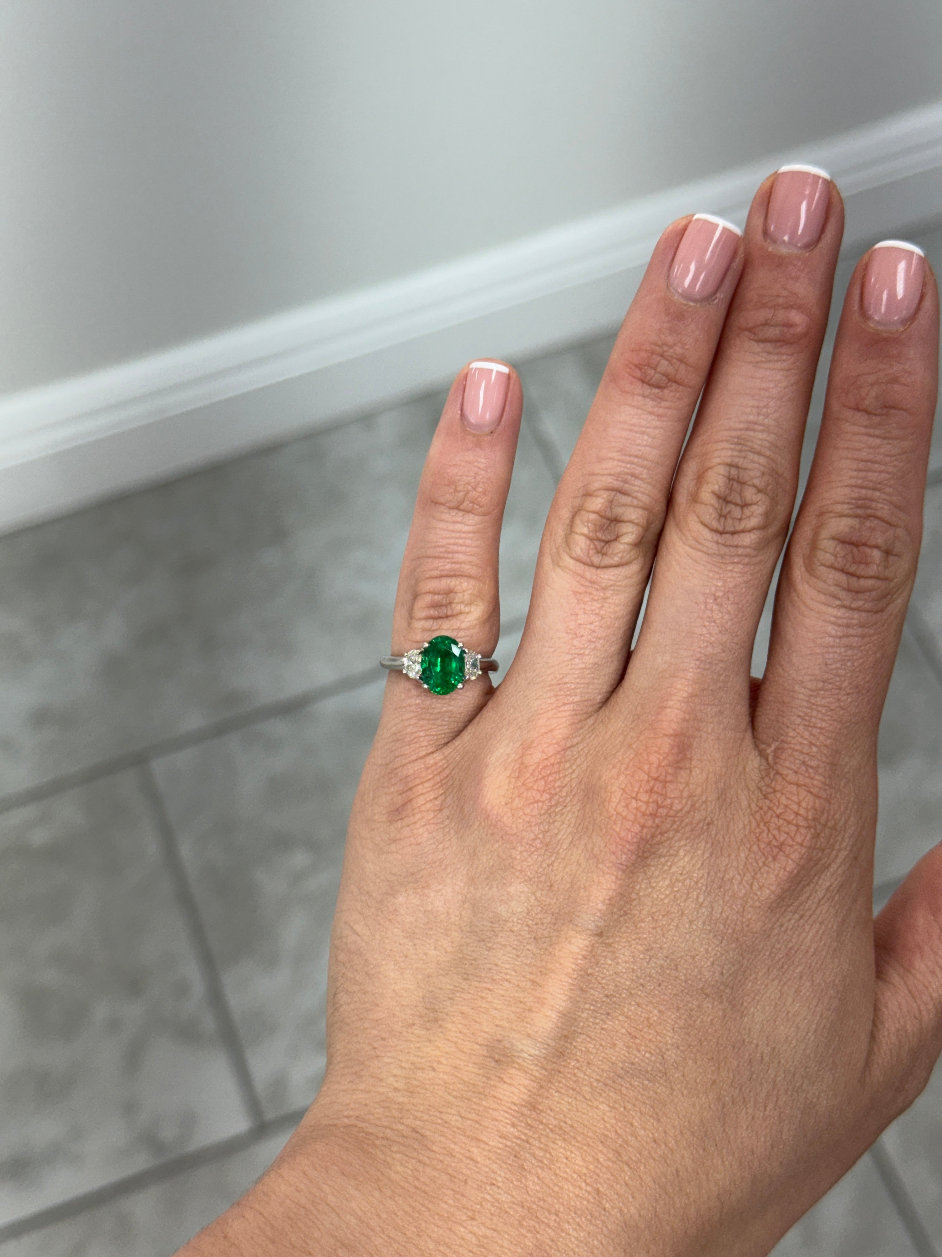 Vivid green oval emerald and diamond three-stone ring in platinum by JR Colombian Emeralds, showcasing sparkling gemstones and elegant design.