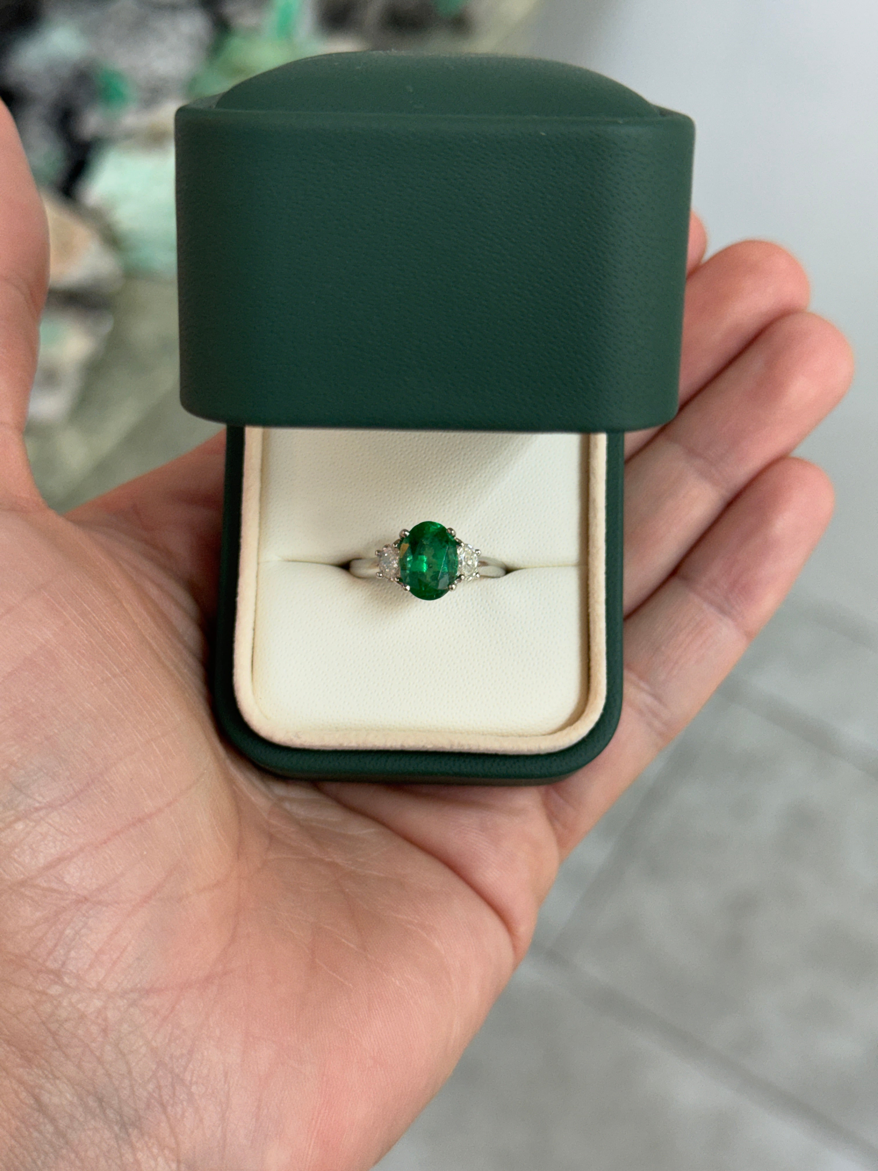 Vivid green oval emerald and diamond three-stone platinum ring by JR Colombian Emeralds, with detailed close-up of the gemstones.