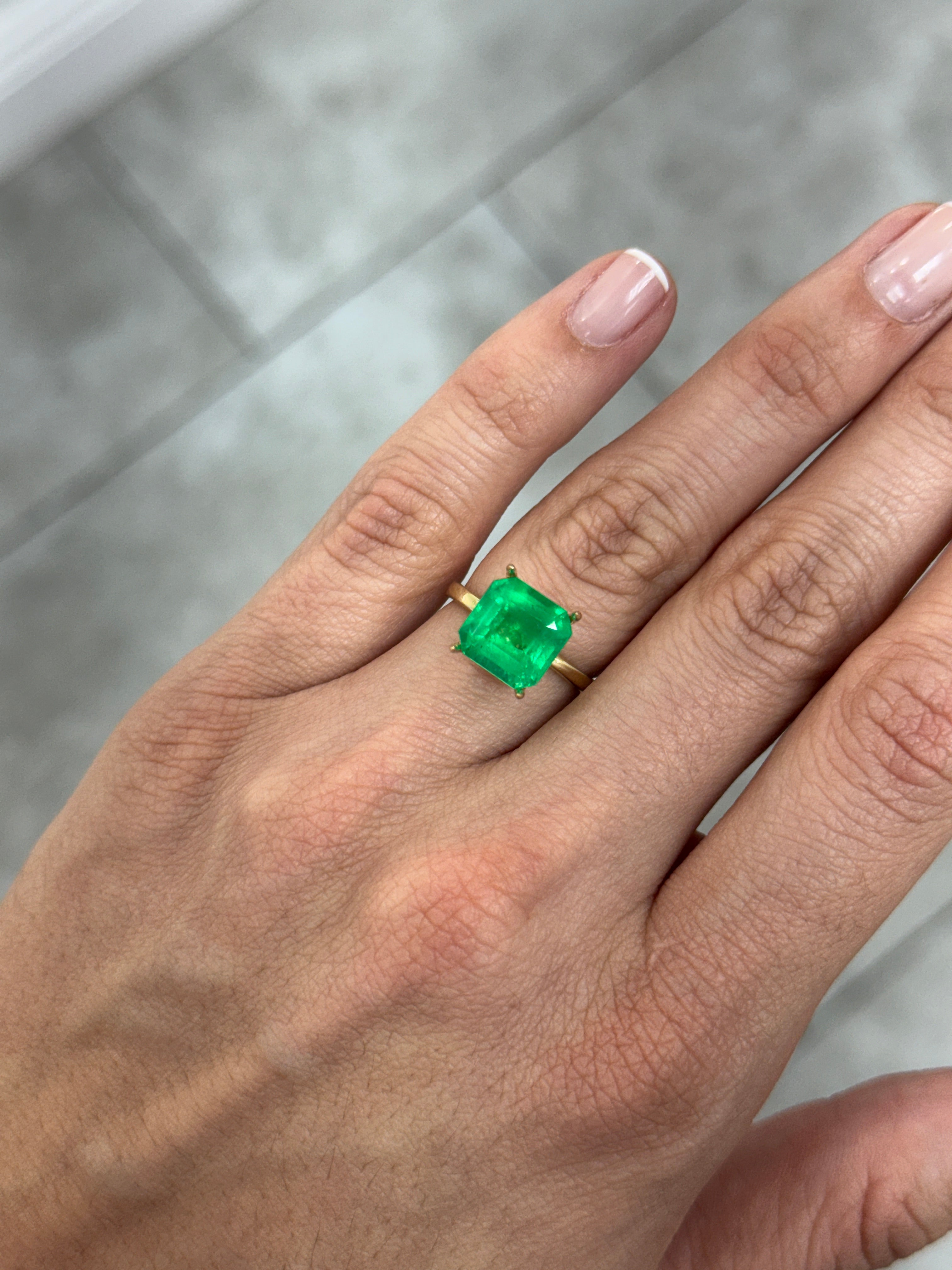 Rectangular 4.35 carat Colombian emerald loose gemstone with kyptonite glow and Asscher cut, displayed on a neutral background.
