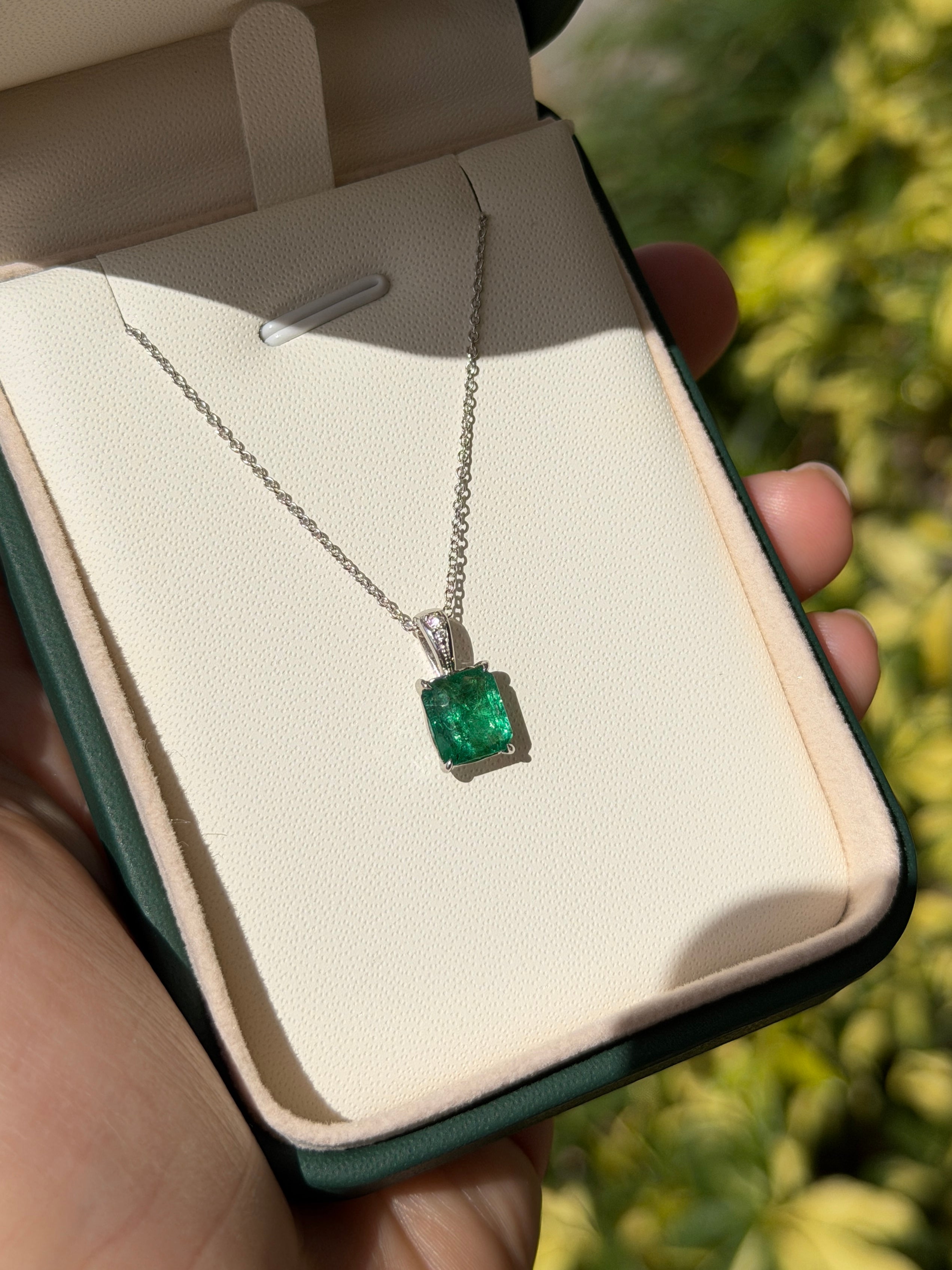 Emerald cut emerald and diamond bail pendant in 14K white gold with 1.60tcw, featuring a central emerald and sparkling diamonds.