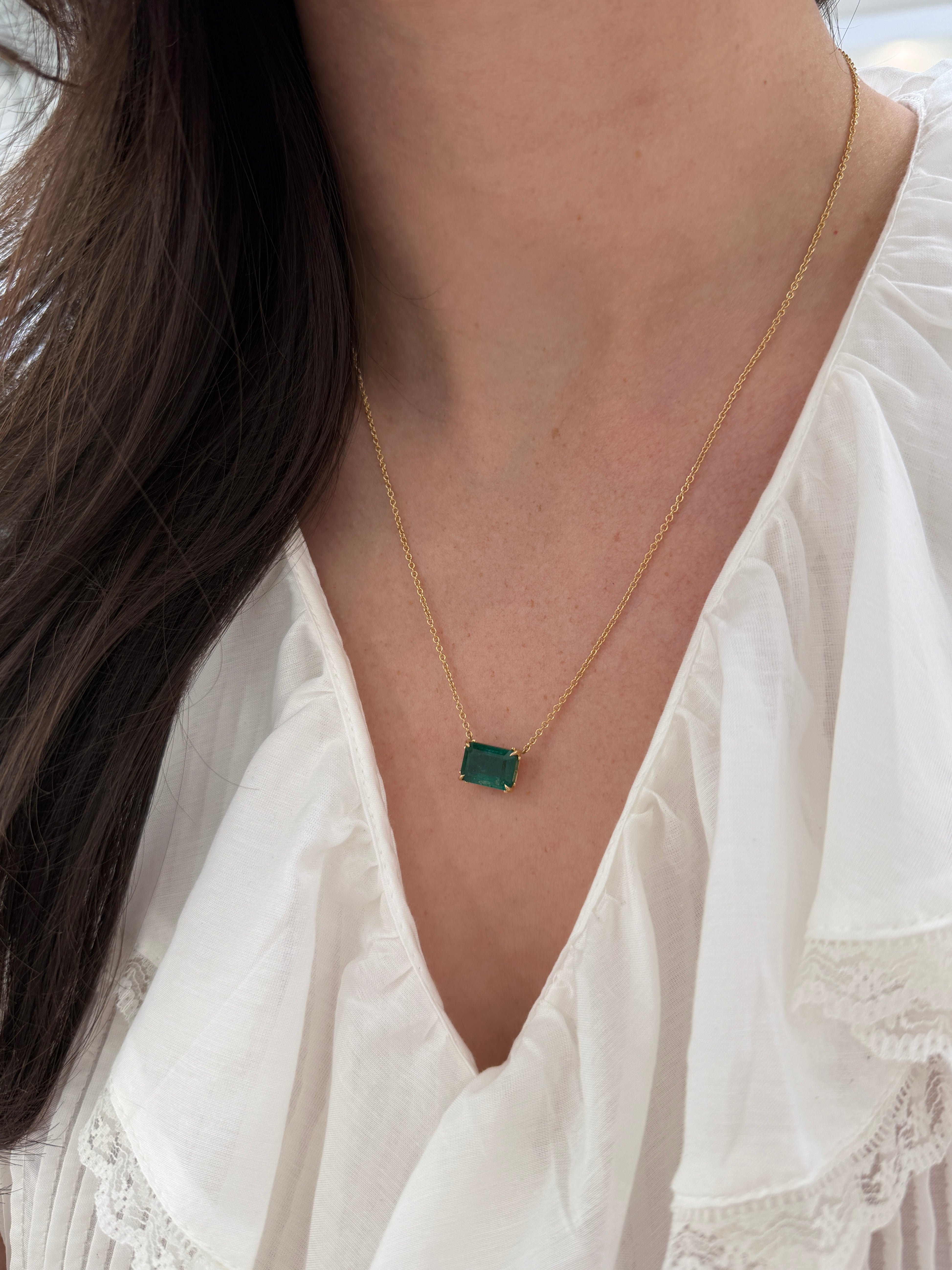 18K gold emerald solitaire necklace featuring a 5.70ct east-west stationary emerald in a fleur de lis design by JR Colombian Emeralds