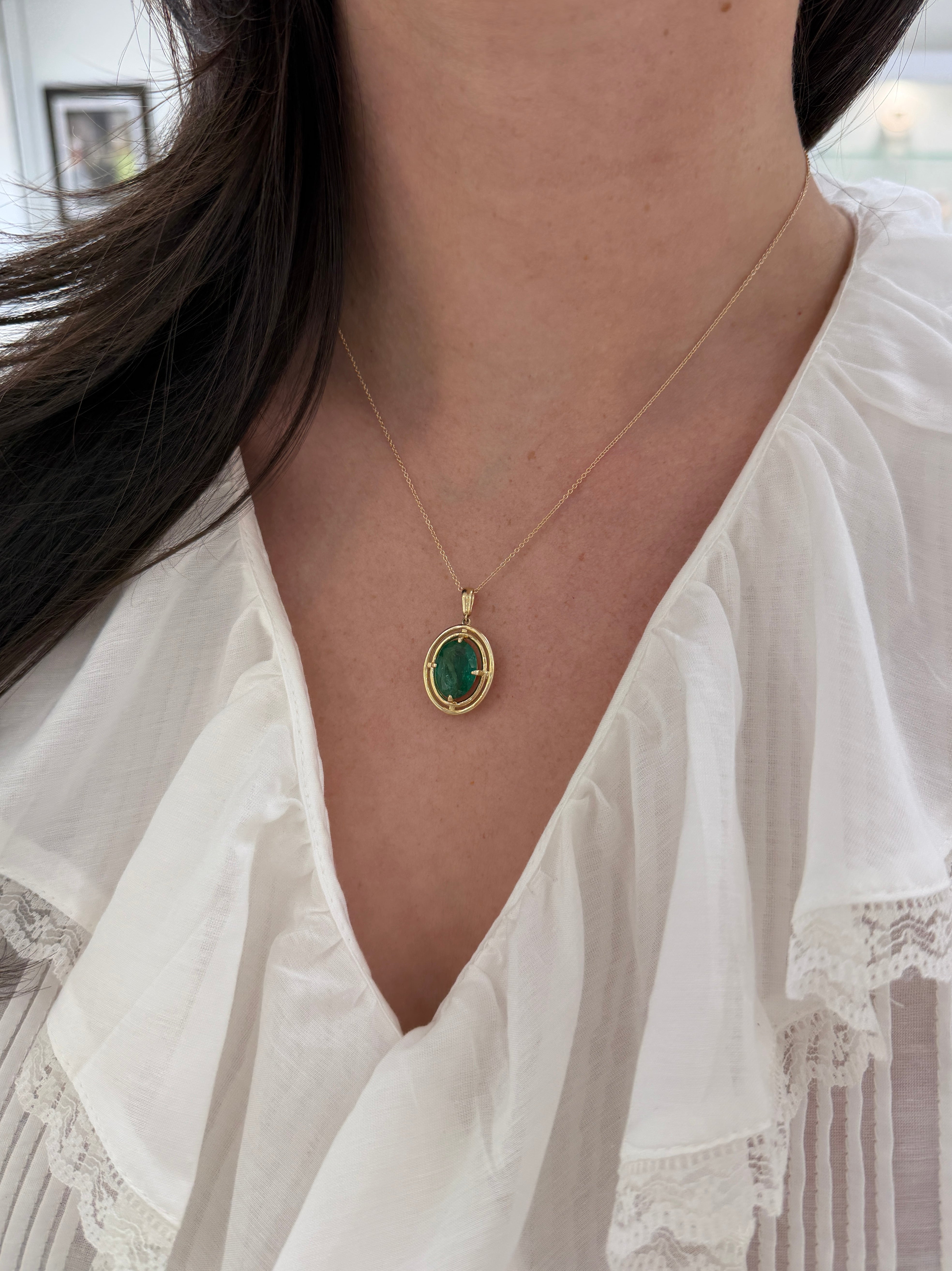 Ciondolo solitario con smeraldo ovale da 5,71 carati e doppio alone in oro giallo 14 carati, con montatura flottante a quattro griffe.