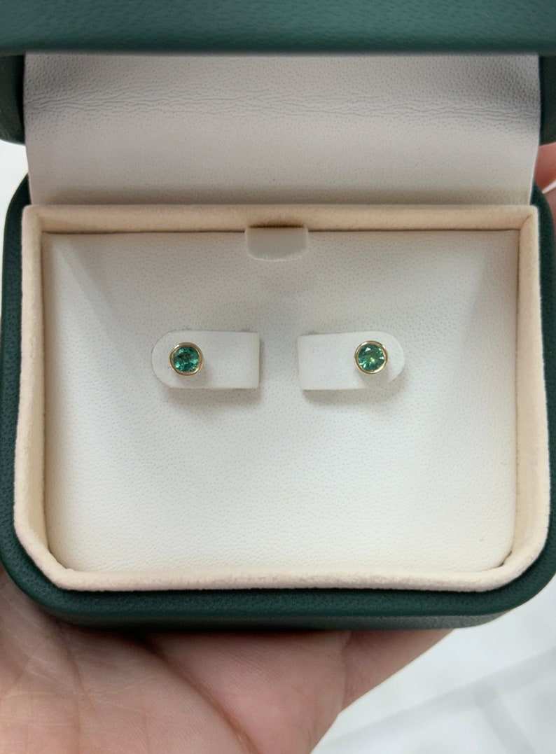 Colombian Emerald 0.50tcw natural green round cut bezel set earrings in 14K yellow gold, showcasing lush green gemstones.