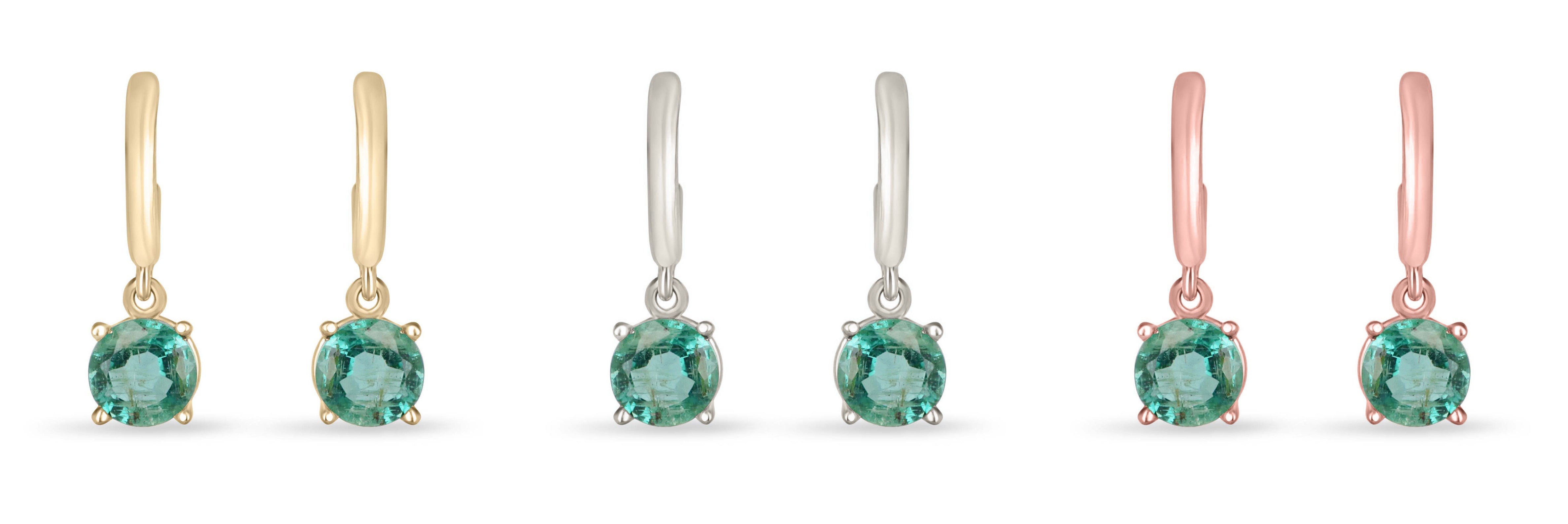 Medium dark green emerald round cut hoop earrings with four prongs in 14K gold, Colombian Emerald brand, shown in close-up photo.