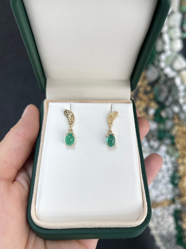 14K yellow gold emerald dangle earrings featuring oval cut green cabochon emeralds and butterfly design.