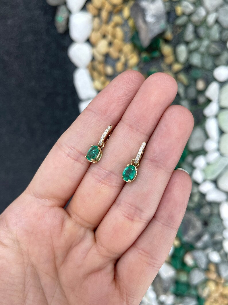 Pair of Colombian Emerald and diamond accent dangle earrings featuring lush green oval-cut emeralds in 14K gold.
