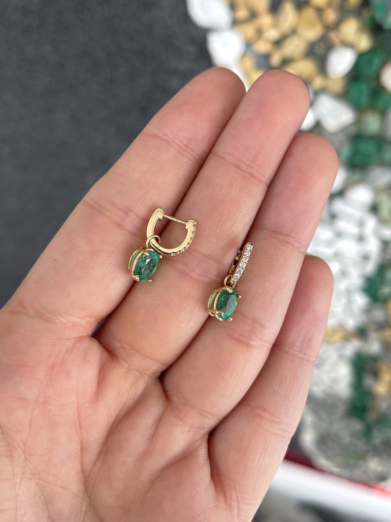 Colombian Emerald and diamond accent dangle earrings with 2.0 tcw lush green oval cut emeralds in 14K gold setting.