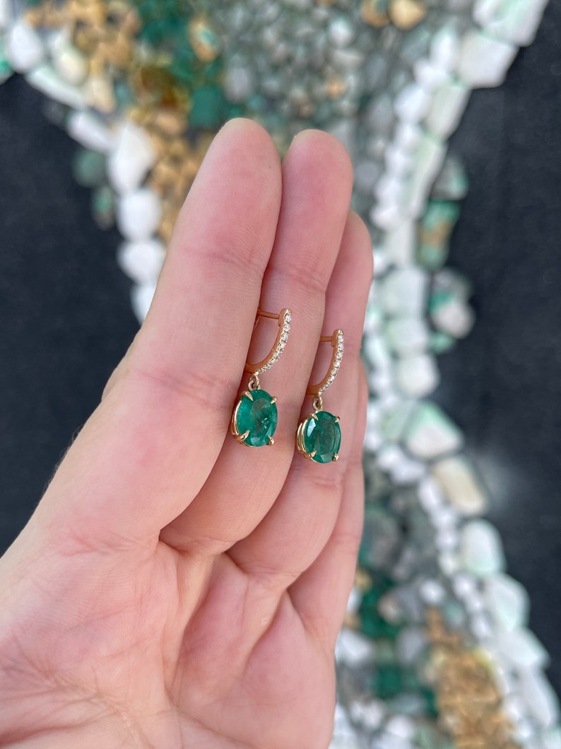 14K gold huggie dangle earrings featuring lush dark green oval cut emeralds and diamond accents.
