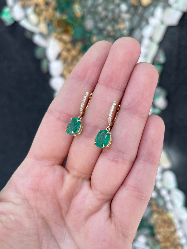 14K gold huggie dangle earrings featuring dark green oval cut emeralds and diamond accents by Colombian Emerald.