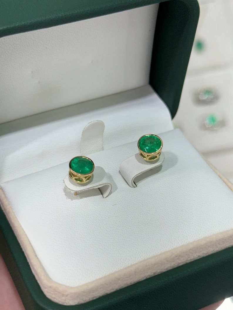 Colombian Emerald earrings featuring 2.14tcw round-cut vivid green emeralds with bezel settings and window accents.