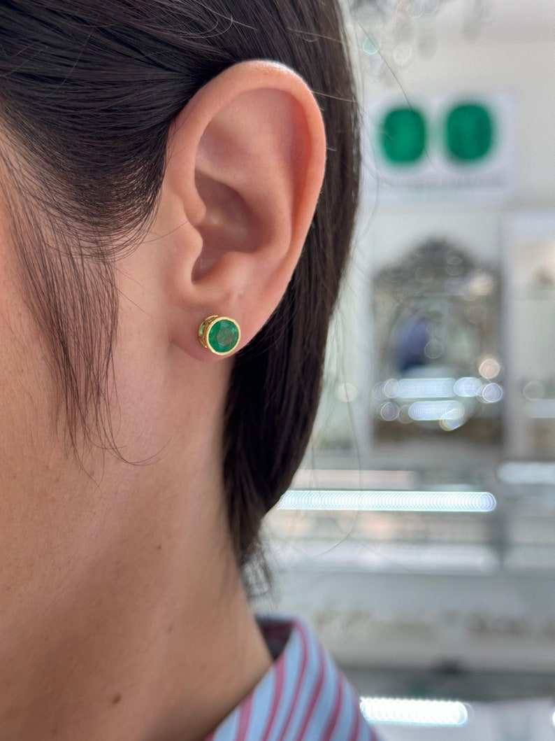 Colombian Emerald earrings with 2.14tcw round cut green emeralds in 18K bezel setting, featuring window design and stud style.