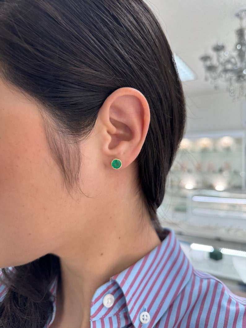 Pair of Colombian Emerald stud earrings with round cut vivid green emeralds in 18K gold bezel settings.
