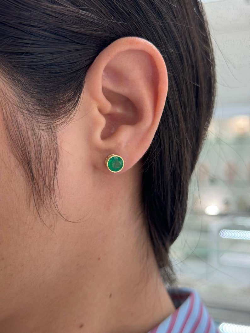 Colombian Emerald earrings with 2.14tcw green round-cut gemstones in 18K gold bezel setting, featuring window accents and emerald studs.