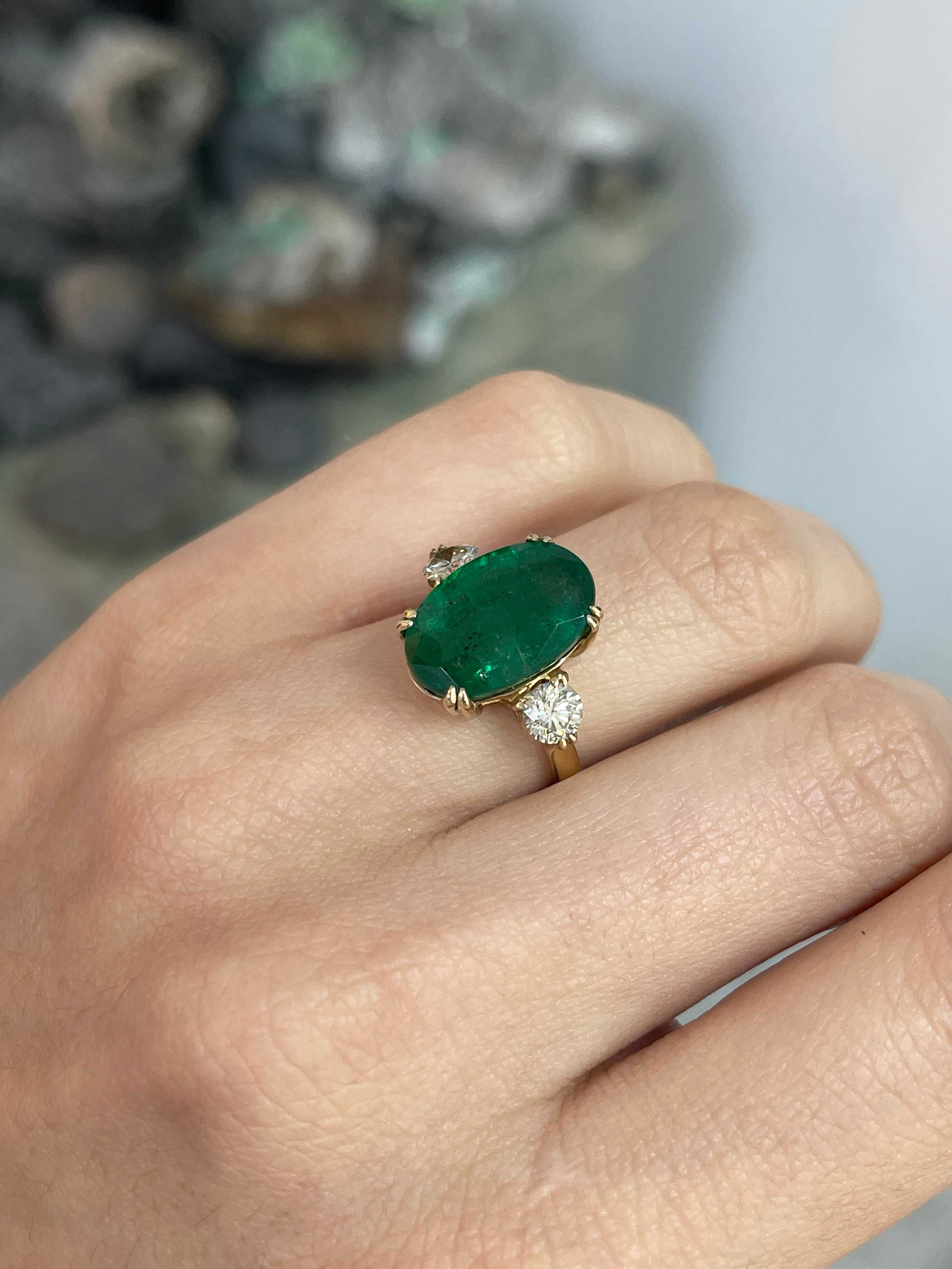 Dark green oval emerald and round diamonds in a 14K Colombian Emerald engagement ring with double prong setting.