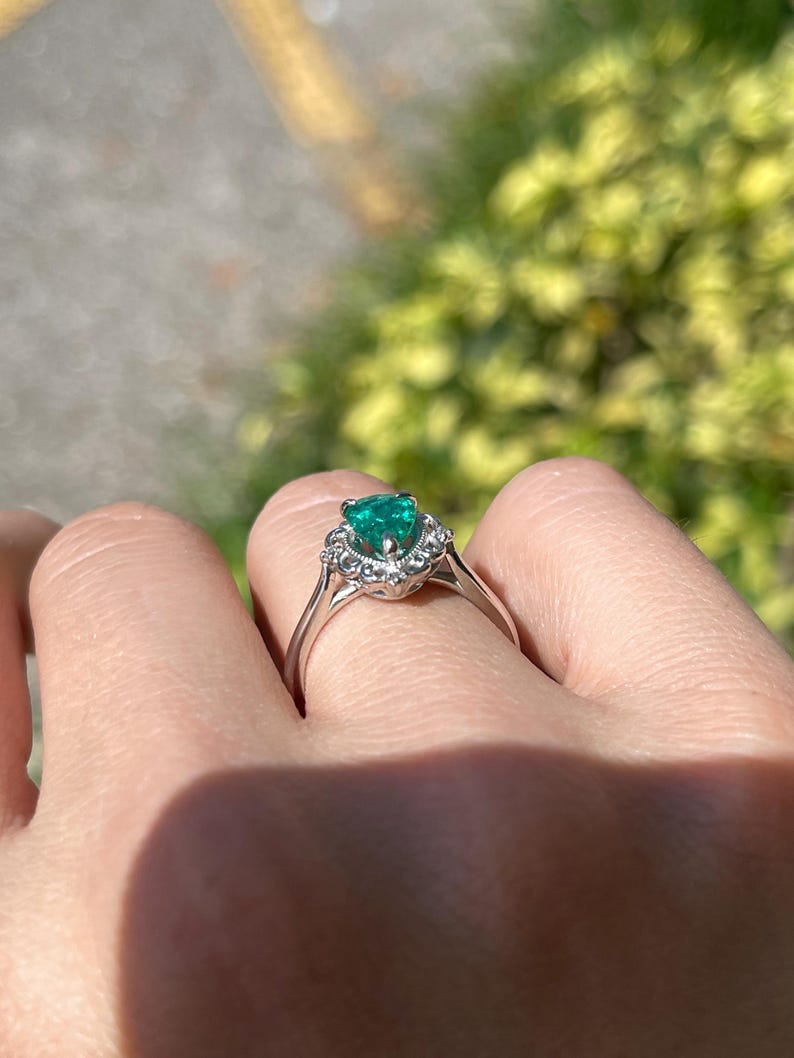 Platinum engagement ring with pear cut emerald, diamond accents, and intricate filigree scroll design by Colombian Emerald.