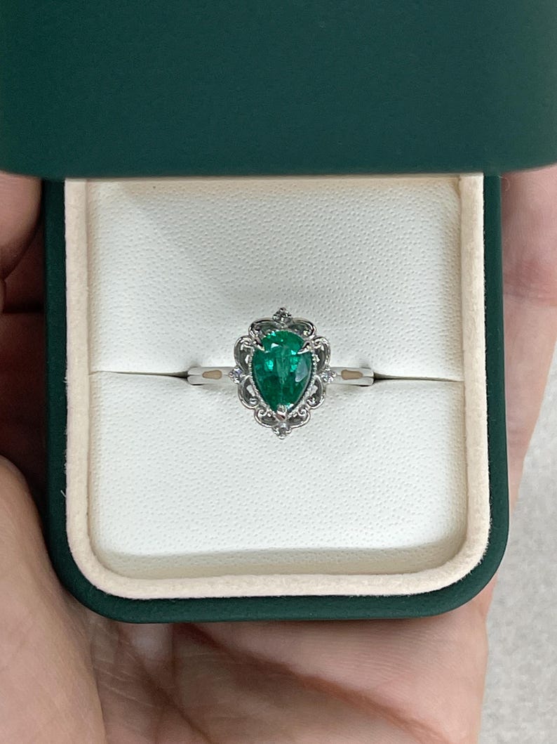 Platinum engagement ring with pear-cut emerald and diamond accents, intricate filigree crown scroll design by Colombian Emerald