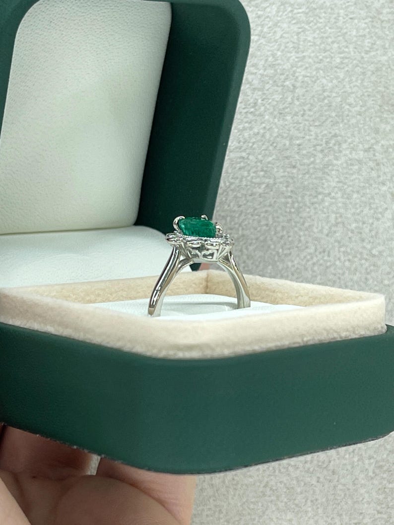 Platinum engagement ring with pear-cut emerald and diamond accents, featuring intricate filigree crown and scroll design.