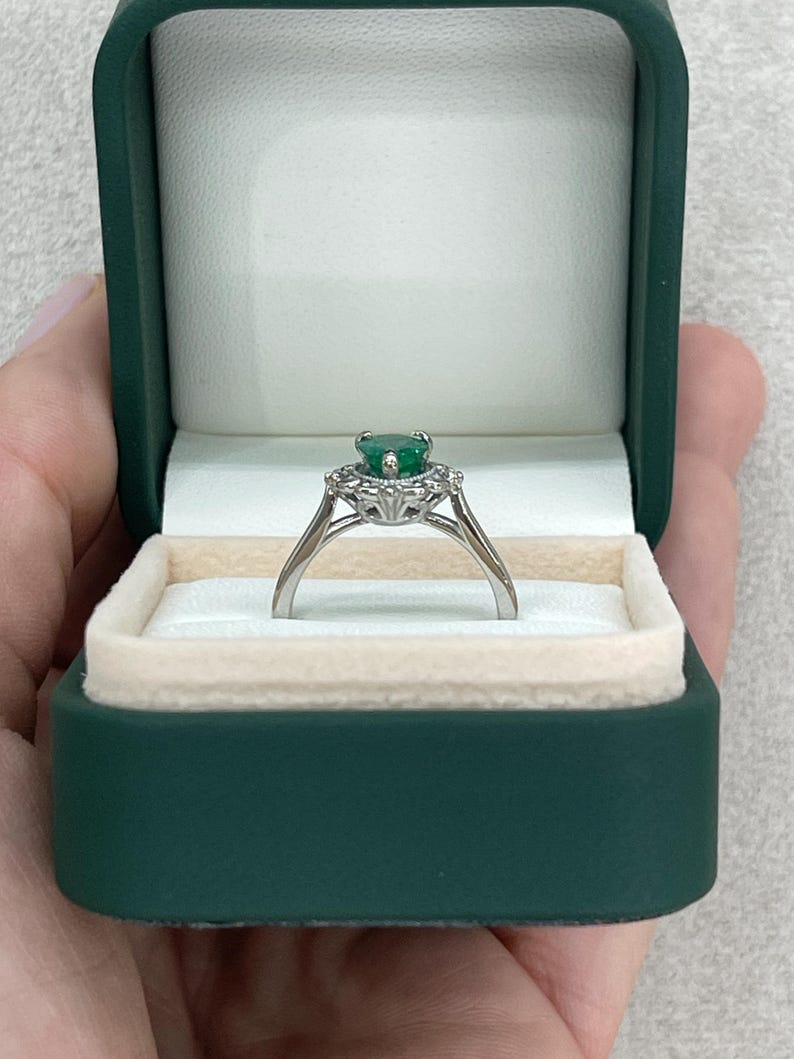 Platinum engagement ring with pear-cut emerald, diamond accents, and intricate filigree crown scroll design.