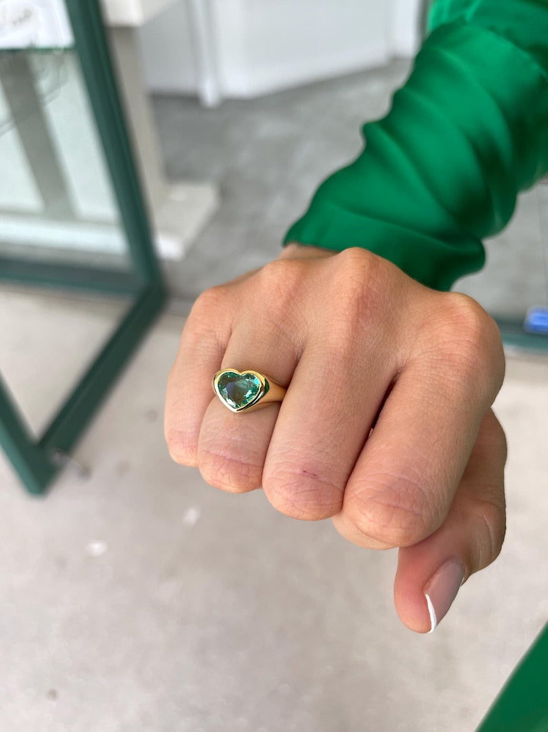 Unisex 18K gold engagement ring with heart-cut Colombian emerald bezel solitaire, featuring a remaining balance label.