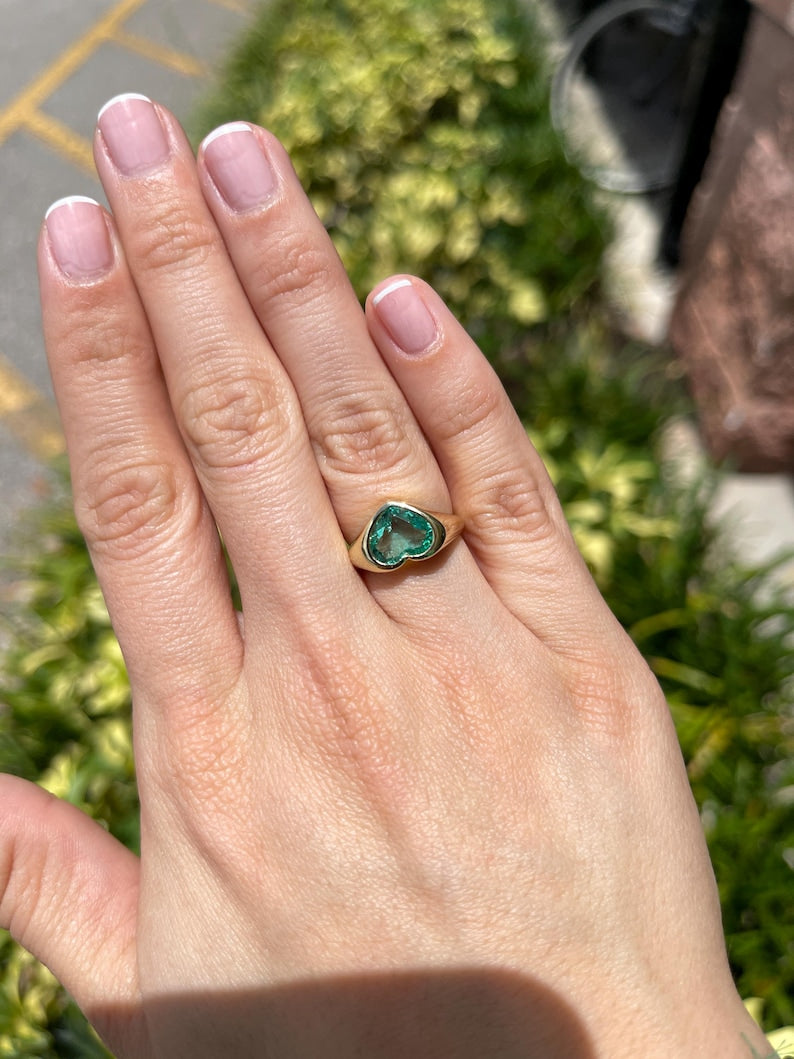 Unisex 18K gold engagement ring with heart-cut Colombian emerald bezel setting, featuring a 2.19ct vibrant green gemstone.