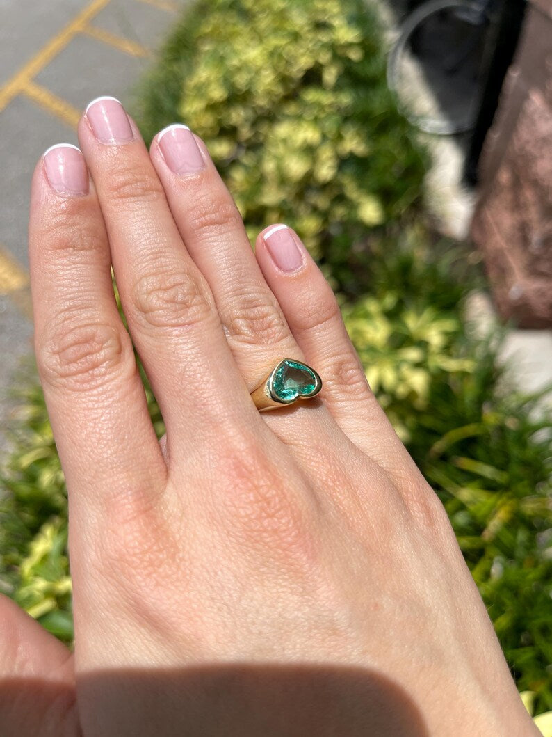Unisex 18K gold engagement ring featuring a heart-cut Colombian emerald bezel setting, designed for Nabil and Tara.