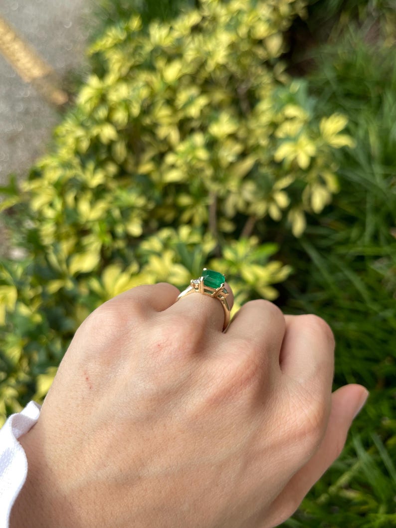 14K green emerald cut and round diamond three-stone engagement ring with Colombian Emerald branding, showcasing elegant gemstone design.