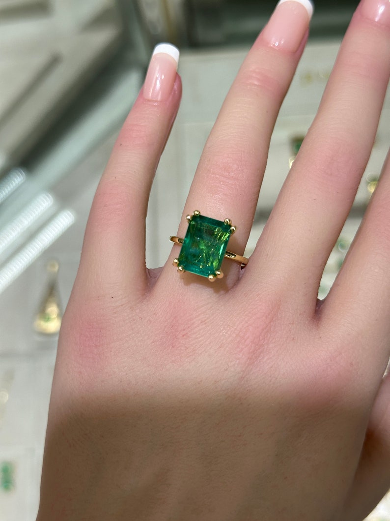 Colombian Emerald 7.35ct 14K gold engagement ring with emerald cut solitaire and chunky claw prongs, showcasing a sparkling green gemstone.