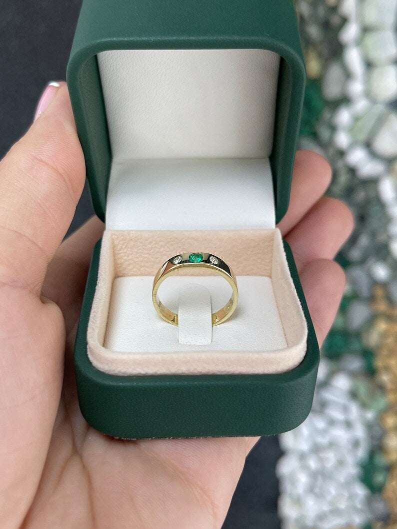 Ladies emerald ring featuring a medium dark green round cut emerald with diamond accents in a 14K three-stone band.