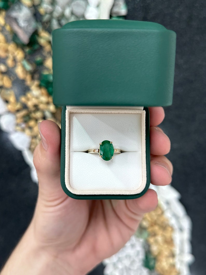14K gold ring with a 2.98ct oval cut forest green emerald solitaire and four-prong setting for right hand wear.