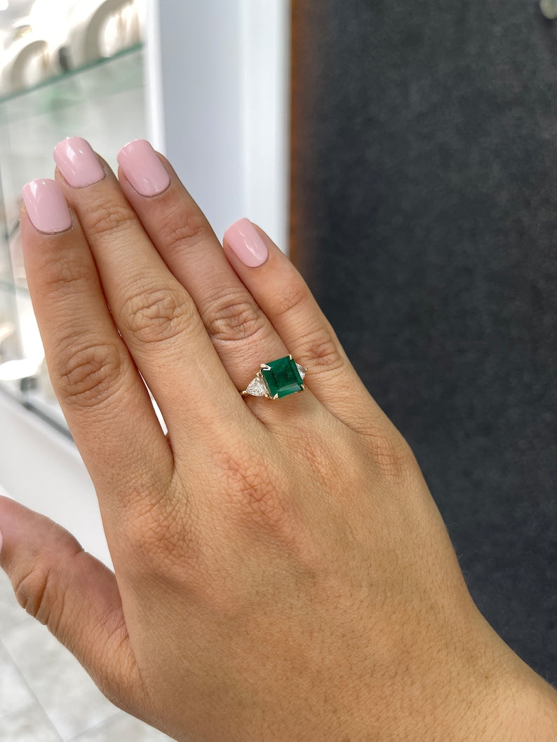 14K gold Colombian Emerald three-stone engagement ring featuring natural trillion and Asscher cut emeralds with diamonds.