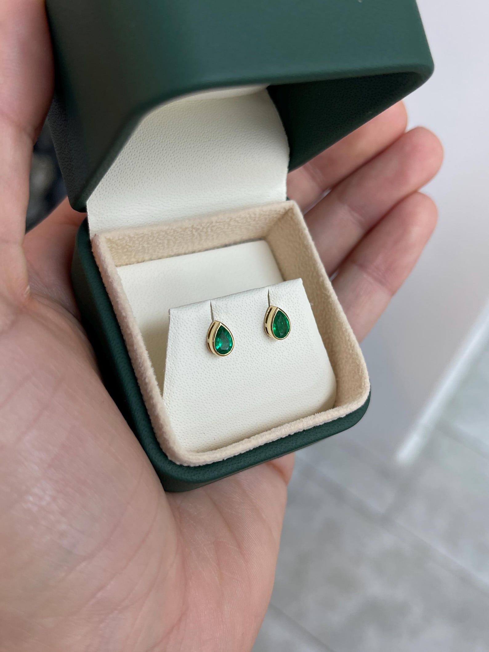 Rich green pear-cut Zambian emerald stud earrings with 18K bezel setting by JR Colombian Emeralds, shown in close-up image.