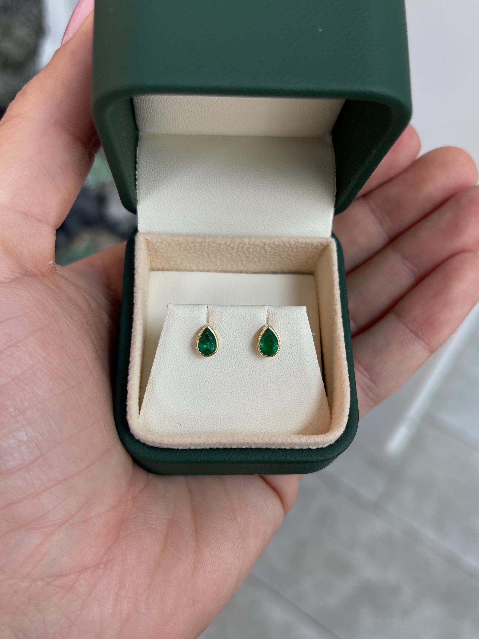 Rich green pear-shaped Zambian emerald stud earrings with bezel setting from JR Colombian Emeralds, showcasing vibrant gemstone detail.
